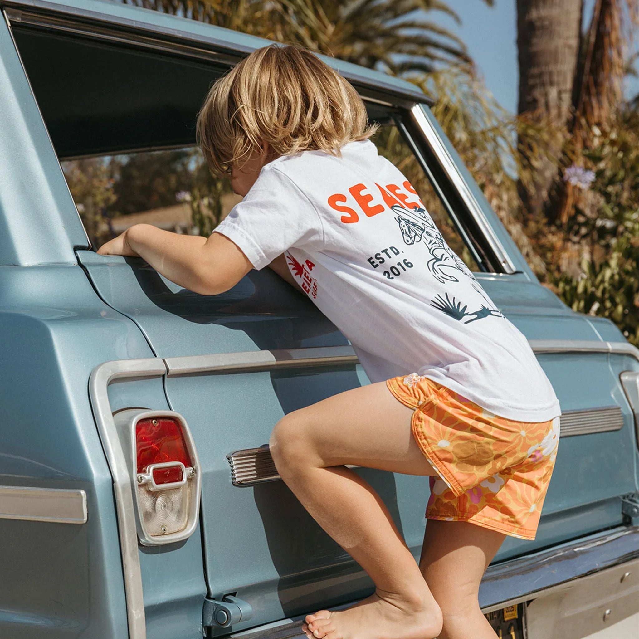 A pair of orange boardshorts with a pink and white flower pattern.