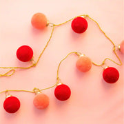 On a peachy pink background is a garland with gold rope and spaced out red and pink flocked glass ball ornaments alternating. 