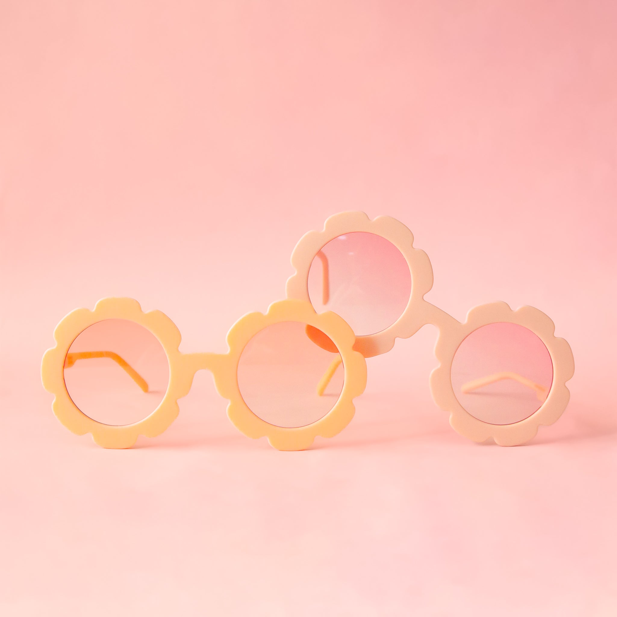 An apricot and pink colored pair of flower shaped sunglasses. Each sold separately. 