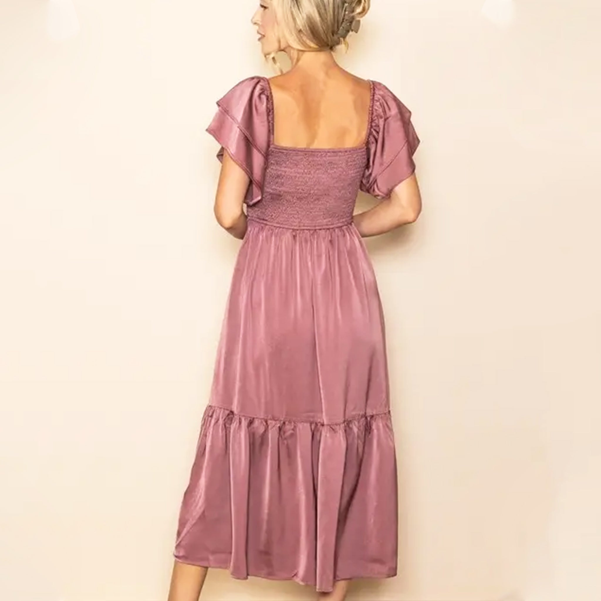 On a cream background is a mauve satin dress with flutter sleeves and side pockets.