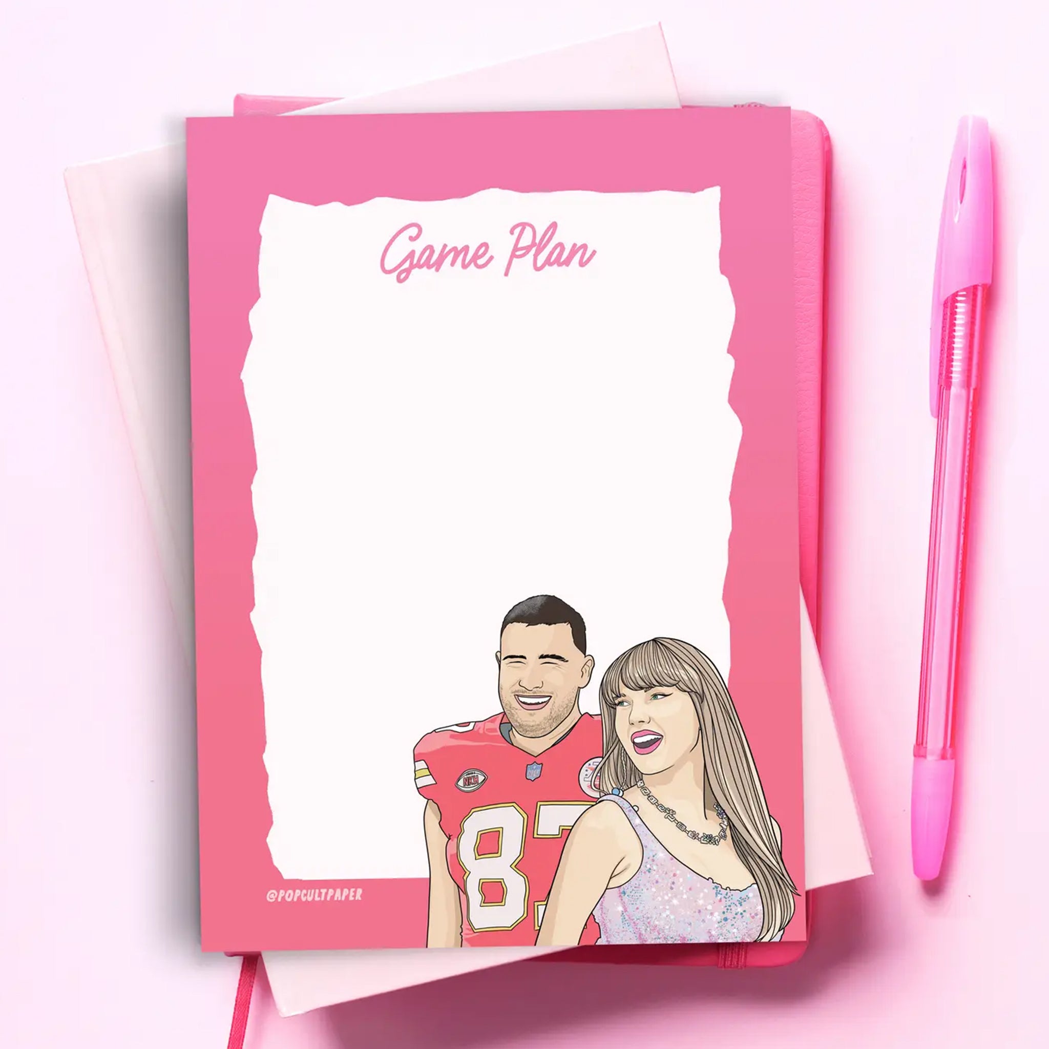 A white notepad with a pink border and illustration of Travis Kelce and Taylor Swift along with pink text that reads, 'Game Plan'. 