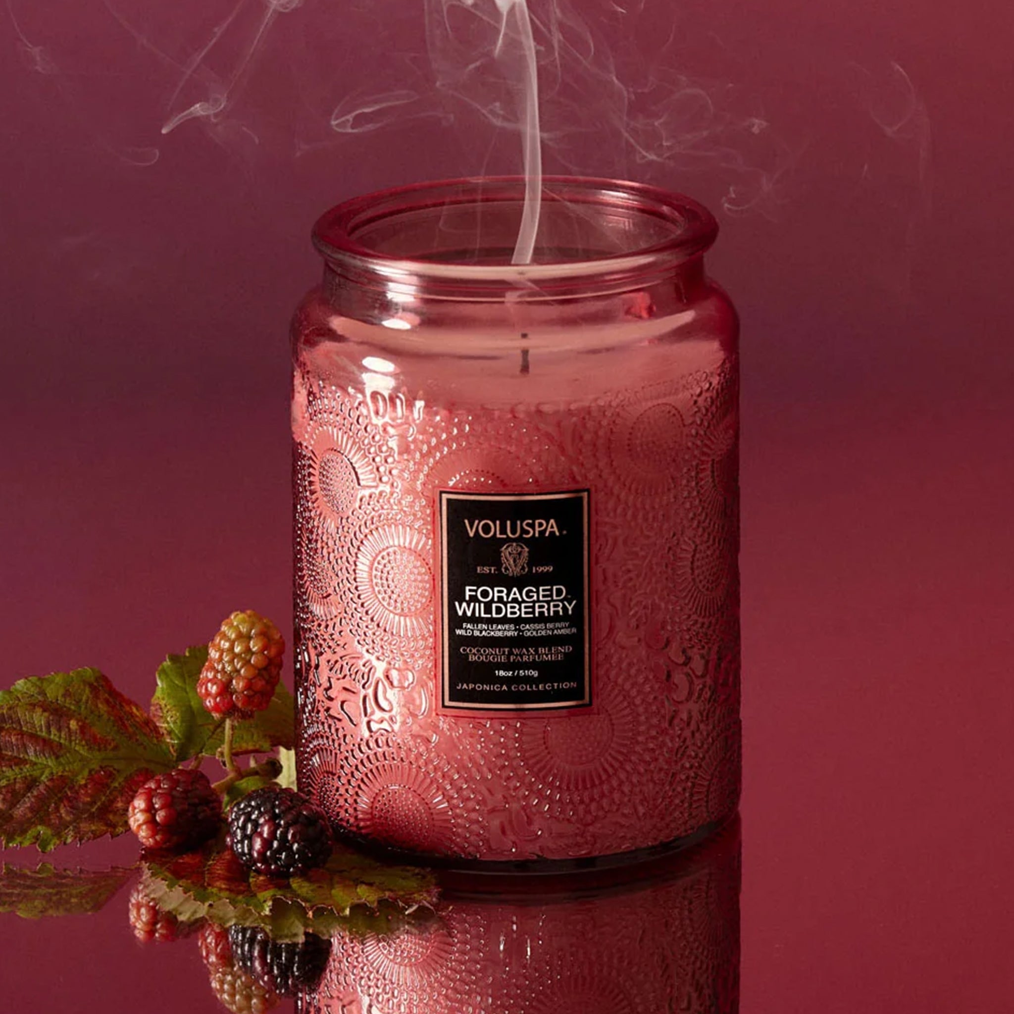 A red decorative glass jar with a black label in the center that reads, &quot;Foraged Wildberry&quot;. 