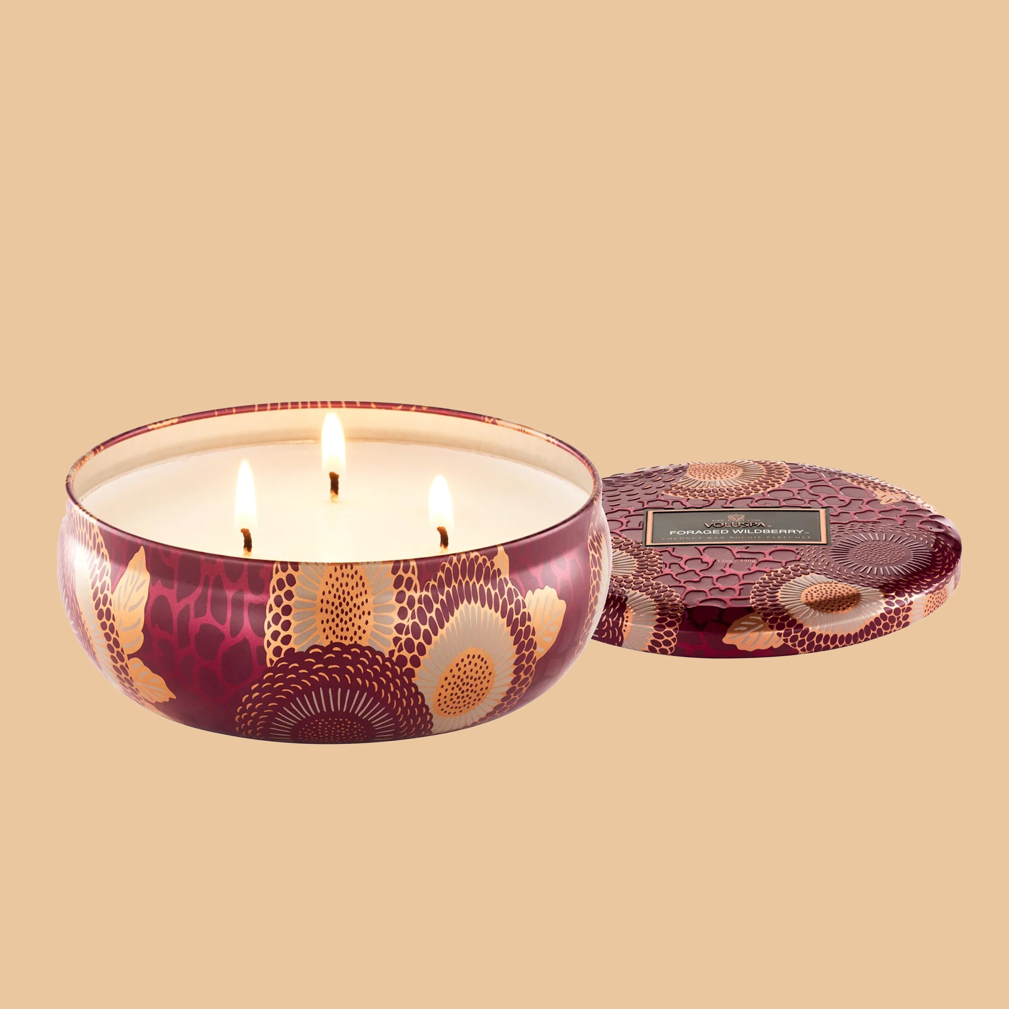 A red and tan floral print metal tin with a three wick candle inside. 