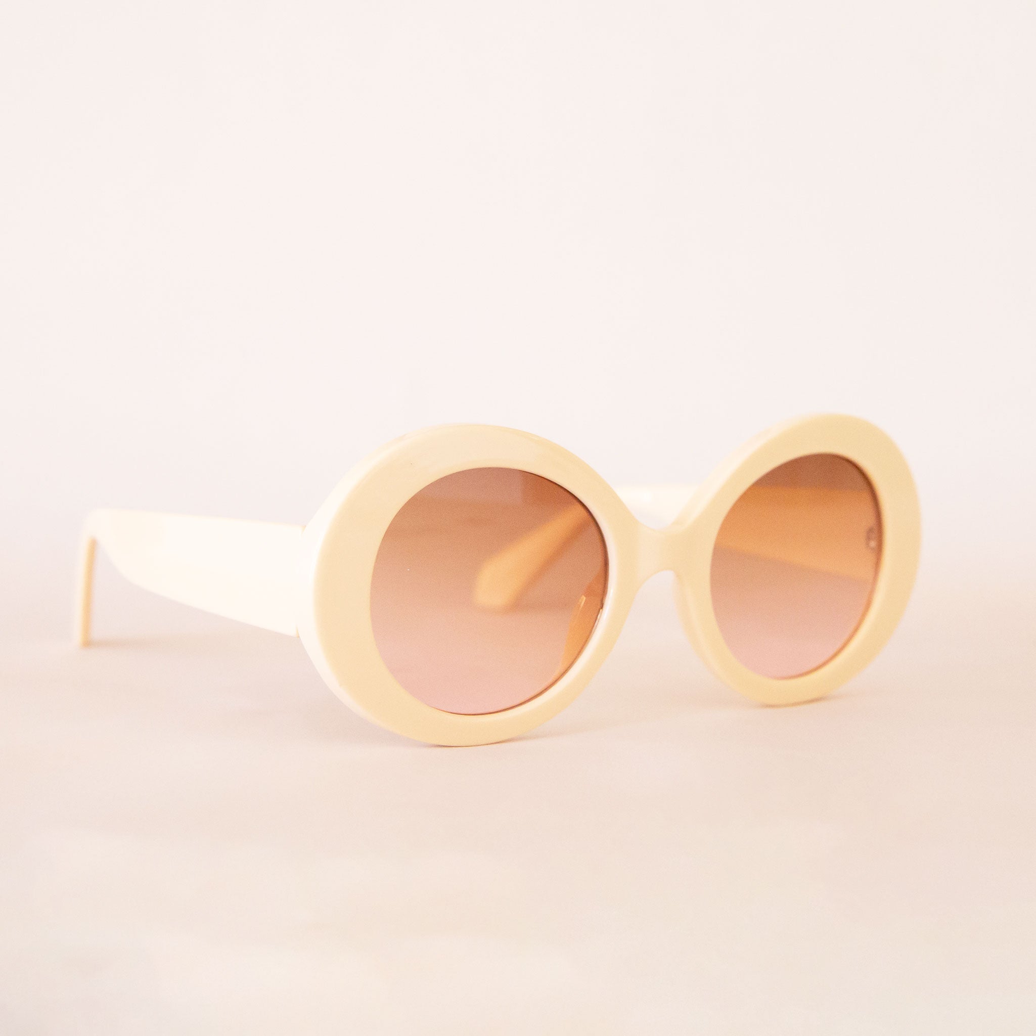 A pair of ivory round sunglasses with a cream/brown lens. 