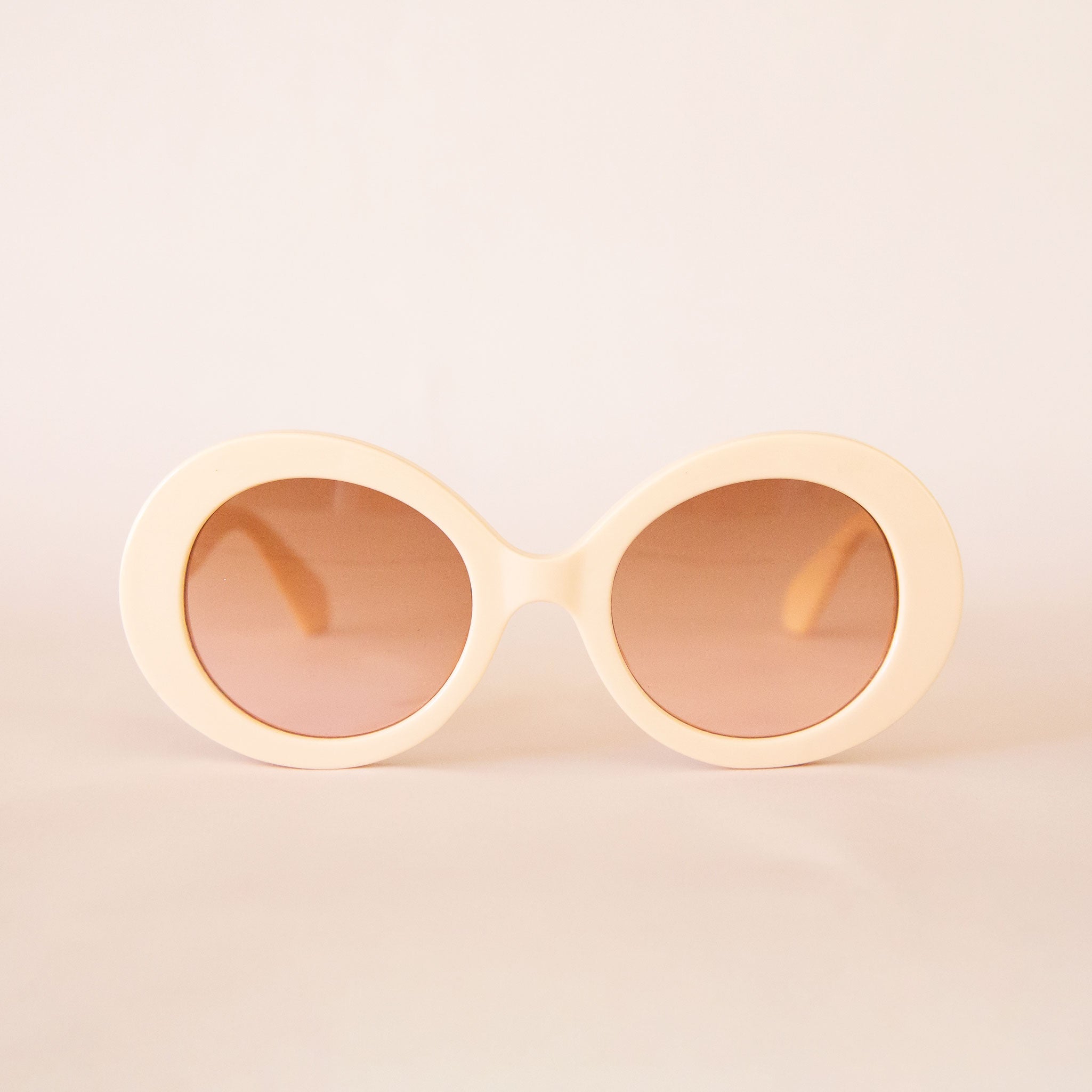 A pair of ivory round sunglasses with a cream/brown lens. 