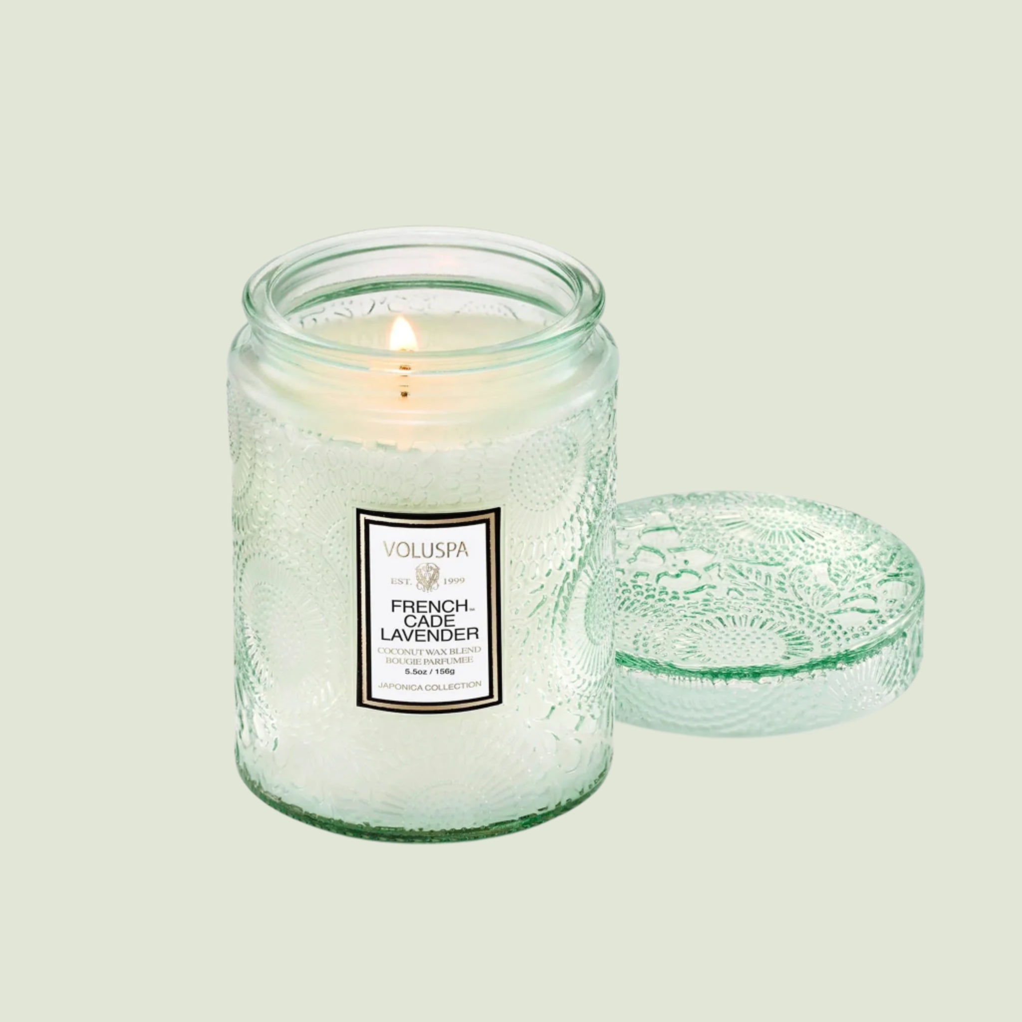 A light green decorative glass jar candle with a white rectangular label that reads, "French Cade Lavender".