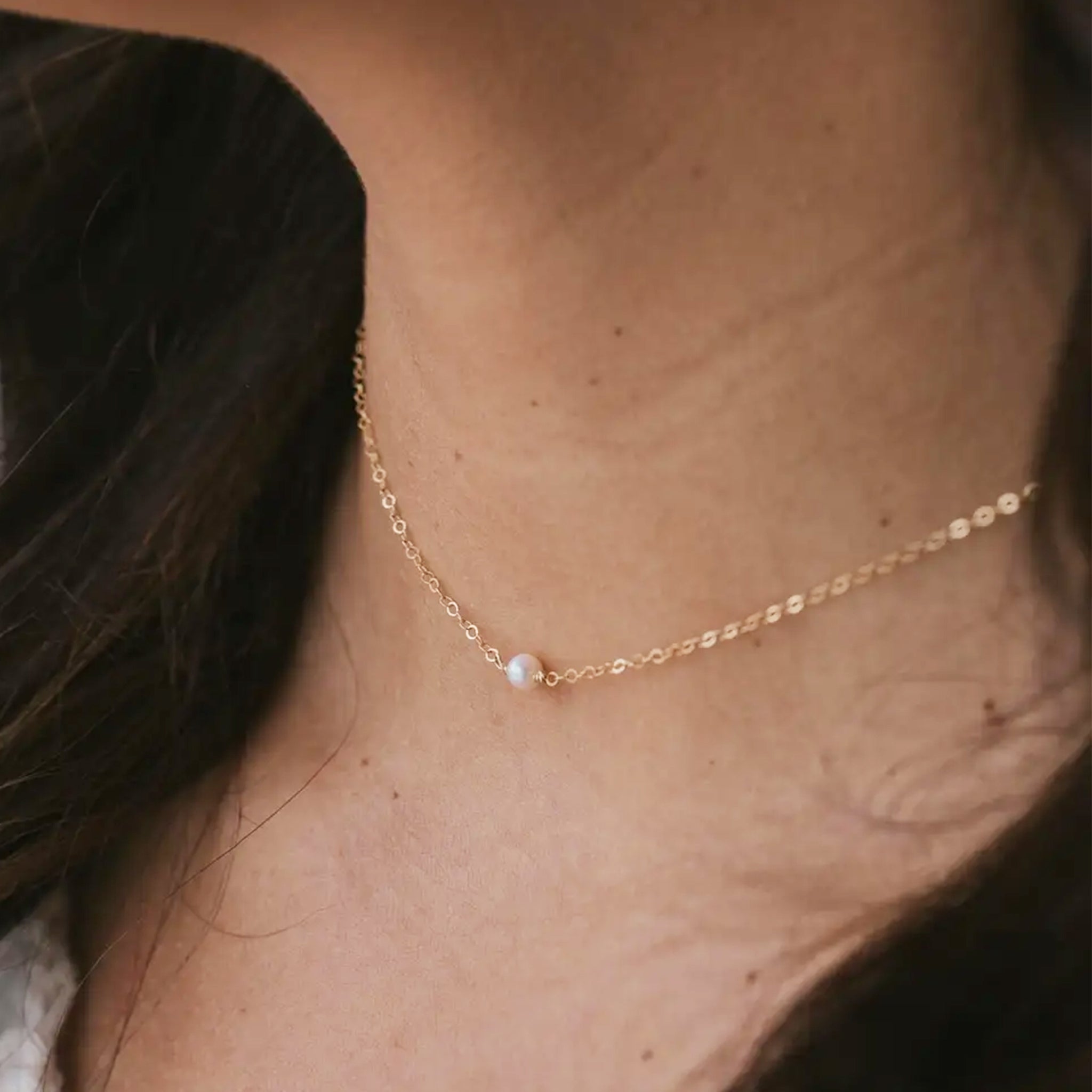 A gold chain necklace with a freshwater pearl in the center. 