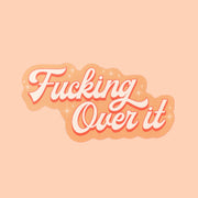 Orange toned sticker that reads 'fucking over it' in light cursive lettering. Small twinkle detailing accents around the text.