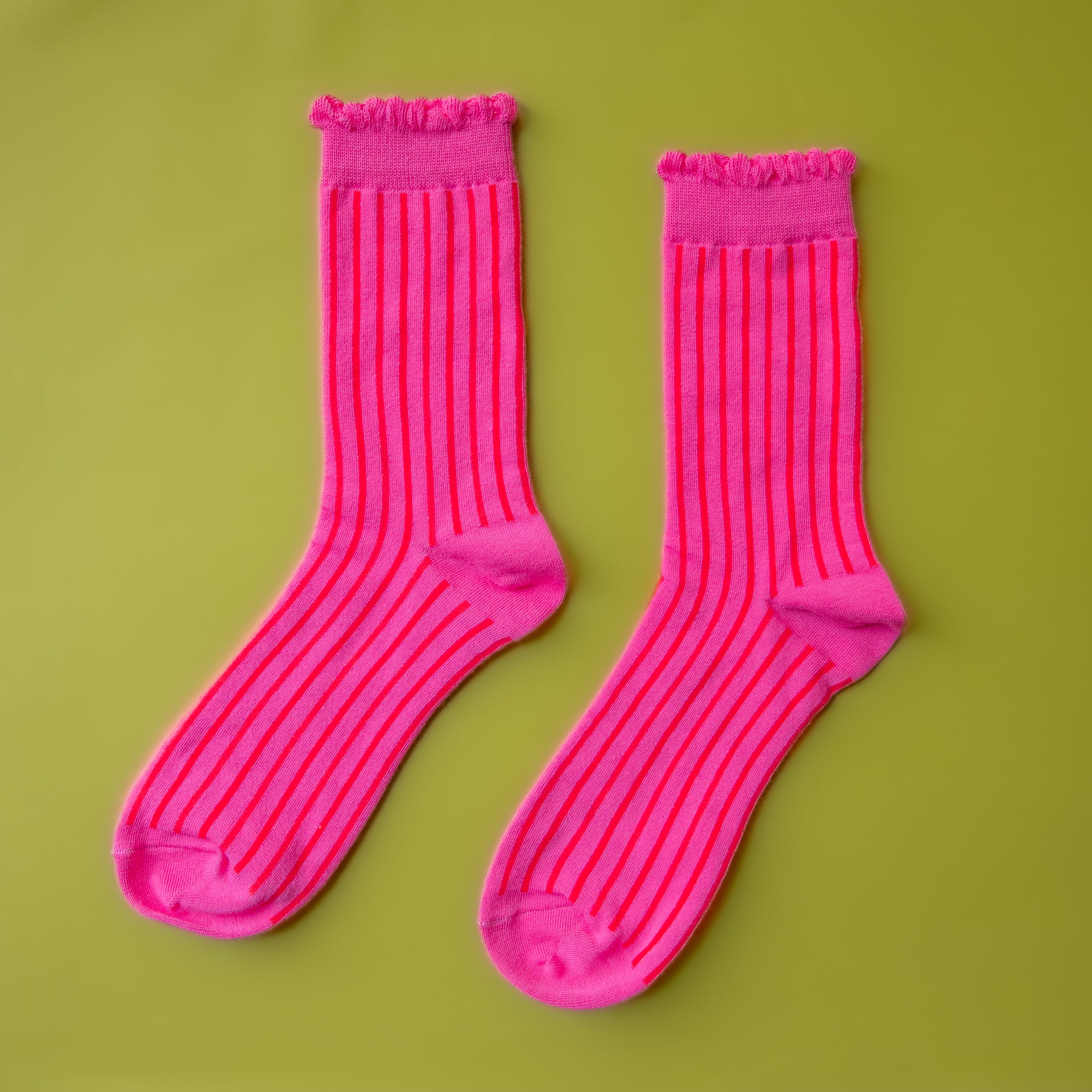 A pair of fuchsia colored striped socks with a ruffle detail at the top. 