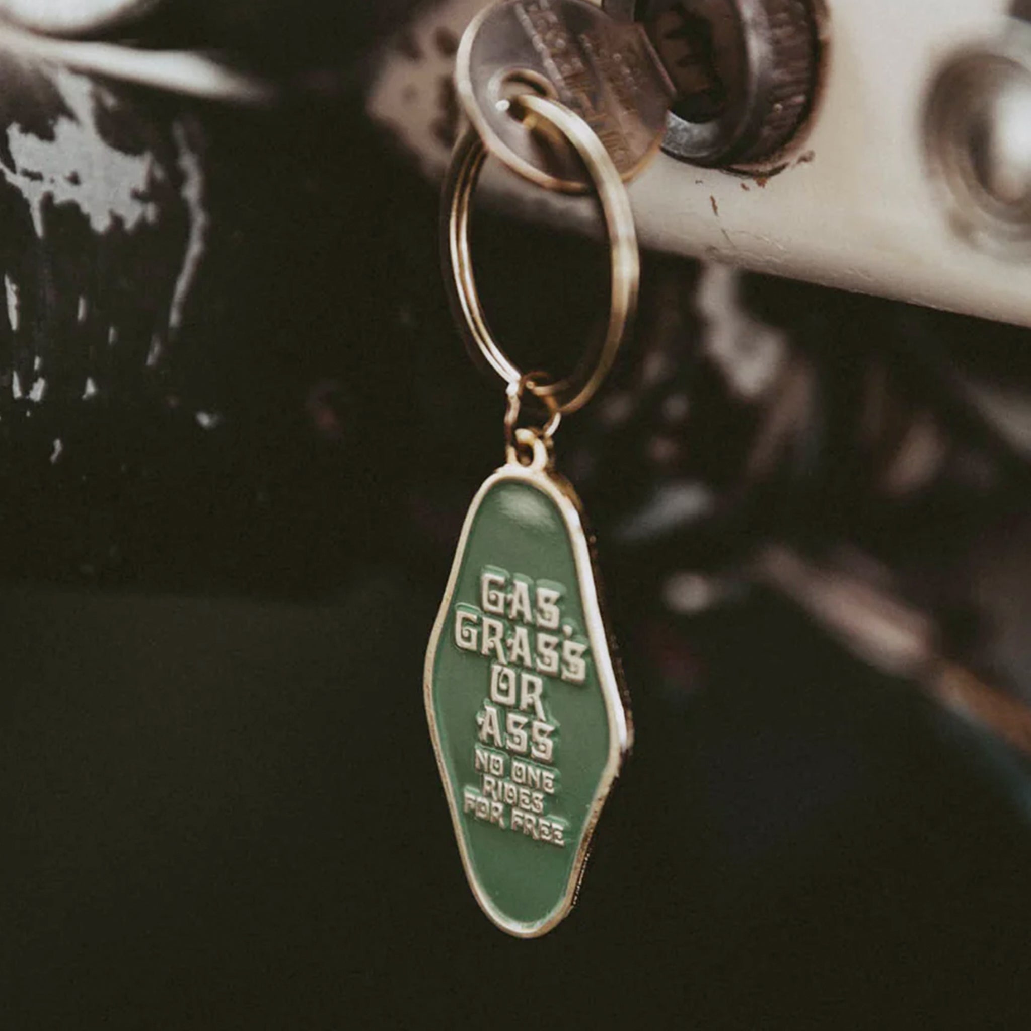 A diamond shaped metal keychain that reads, &quot;Gas, Grass or Ass No Ones Rides For Free&quot; along with a gold loop at the top to attach to keys. 