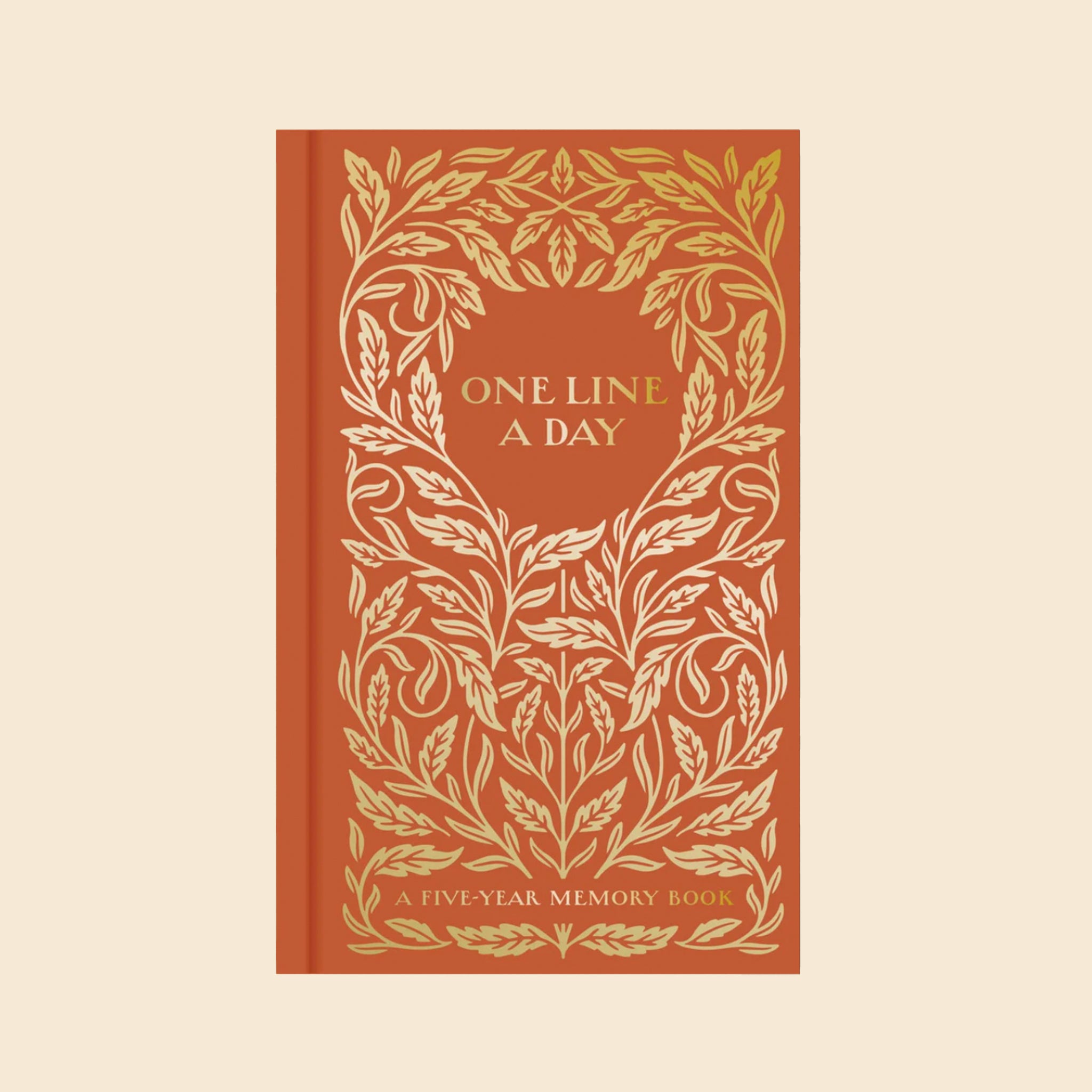 An orange journal with gold foiled foliage design and text in the circle that reads, "One Line A Day". 