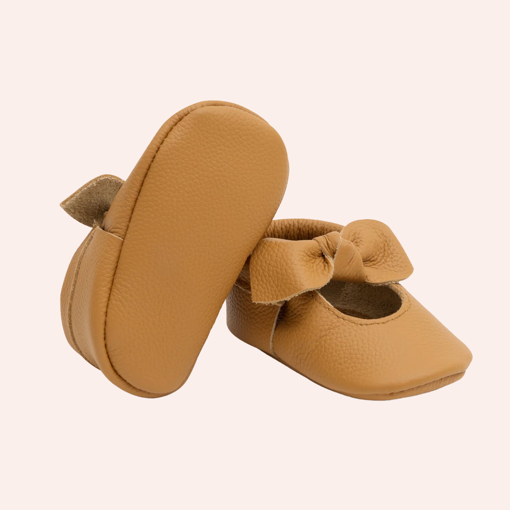 A pair of brown leather moccasins for children with a bow knot detail. 