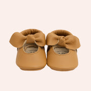 A pair of brown leather moccasins for children with a bow knot detail.