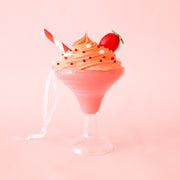 A pink and clear cocktail shaped ornament with a whipped topping and a red and white striped straw with a ribbon loop for hanging. 