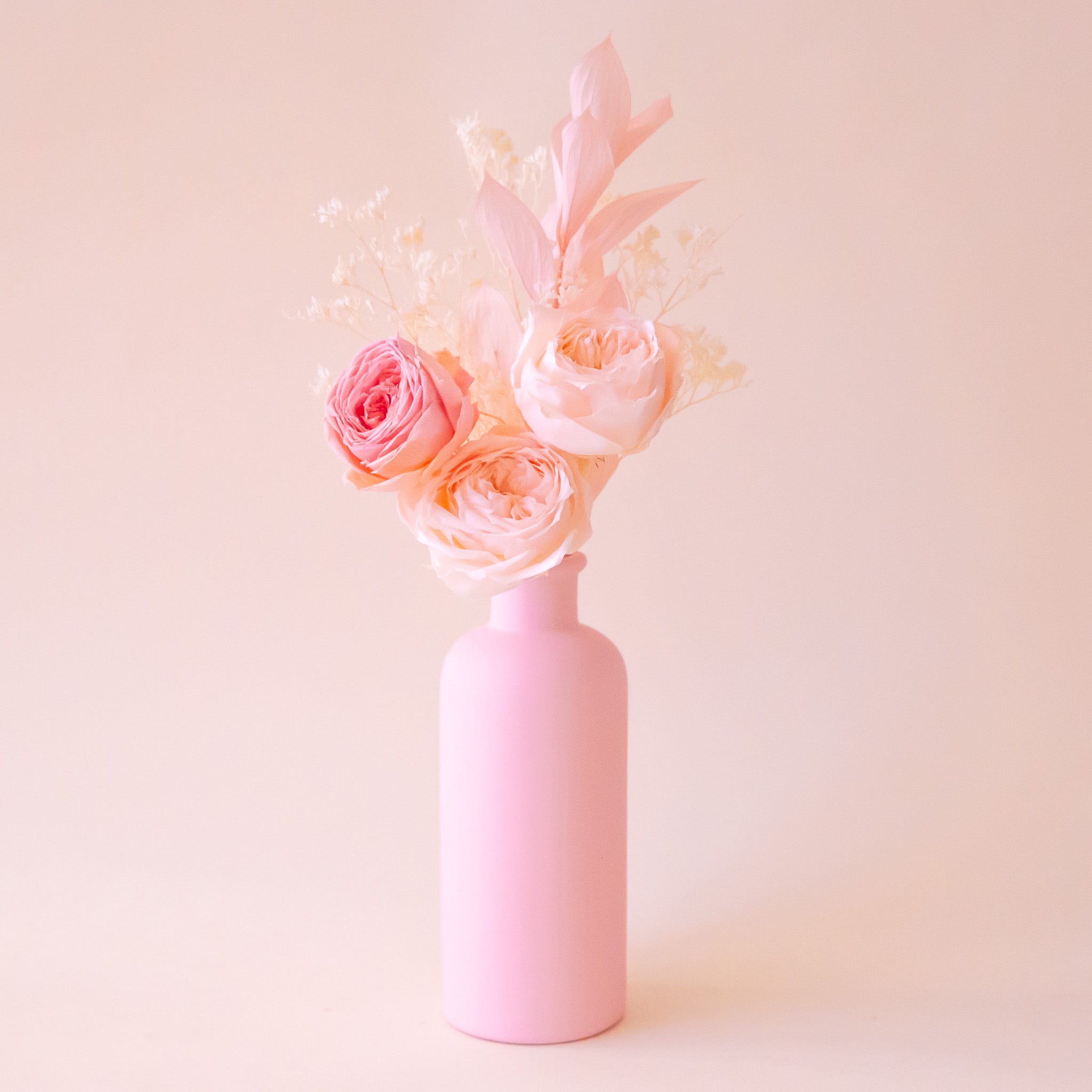 A ceramic light pink bottle neck vase with dried florals inside. 