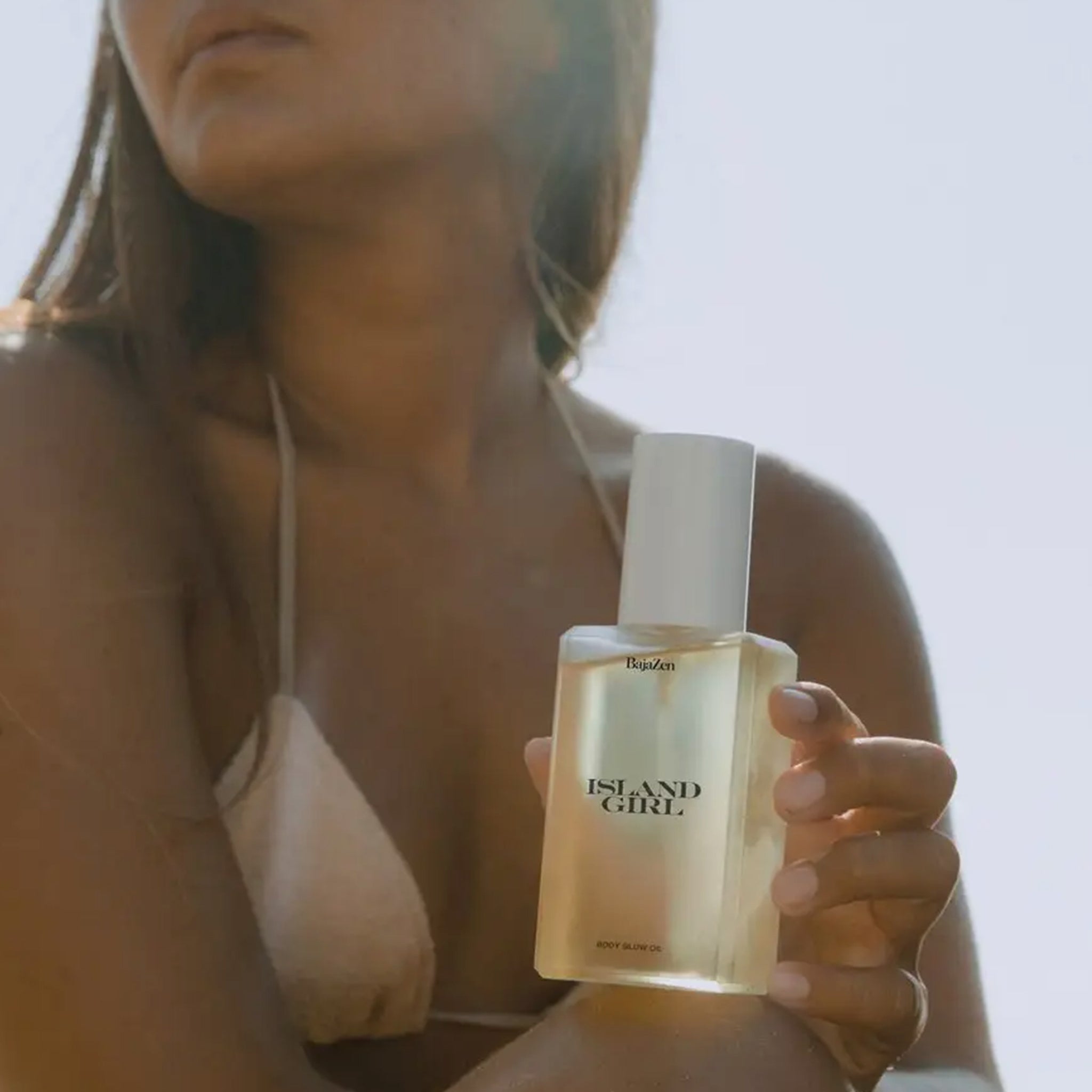 A clear container of body glow oil with a white pump lid and black text that reads, &quot;Island Girl&quot;.