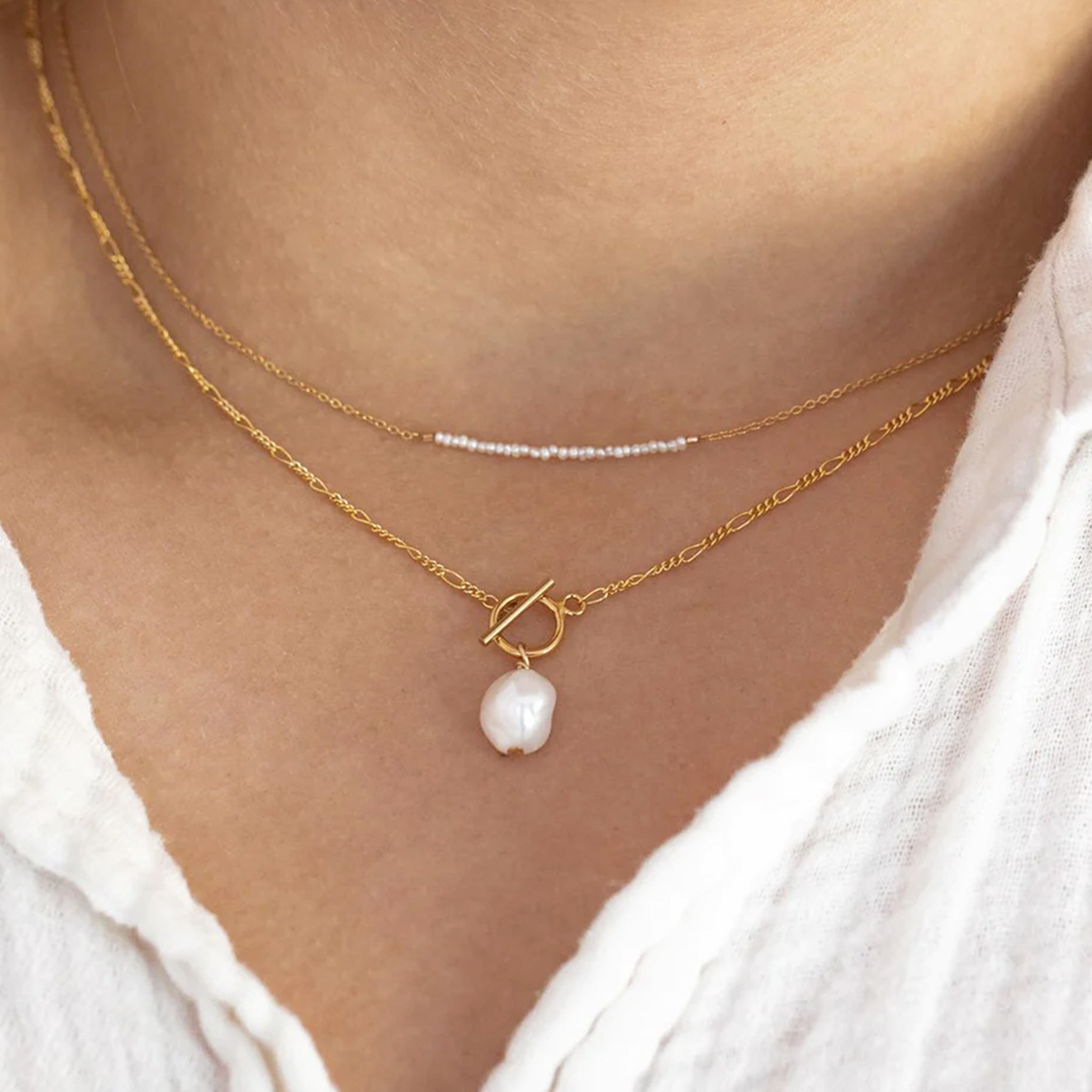 A gold chain necklace with a stack of tiny pearl beads horizontal along the chain. 