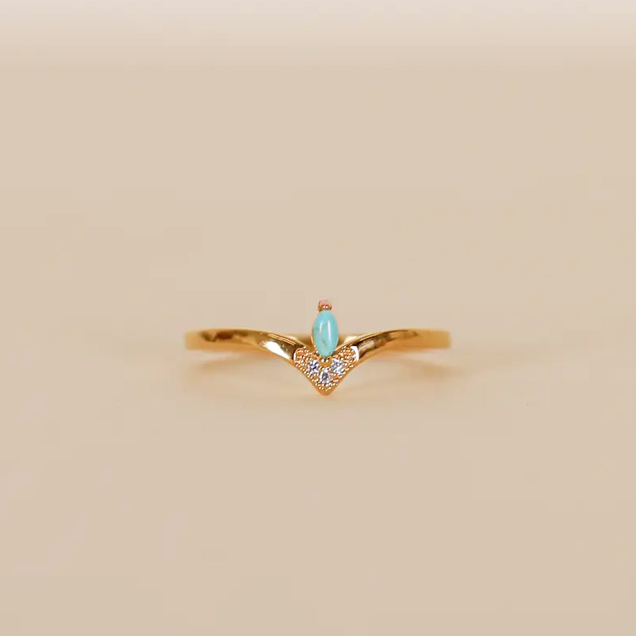 A gold ring with a turquoise stone in the center and cz accents around the bottom point. 