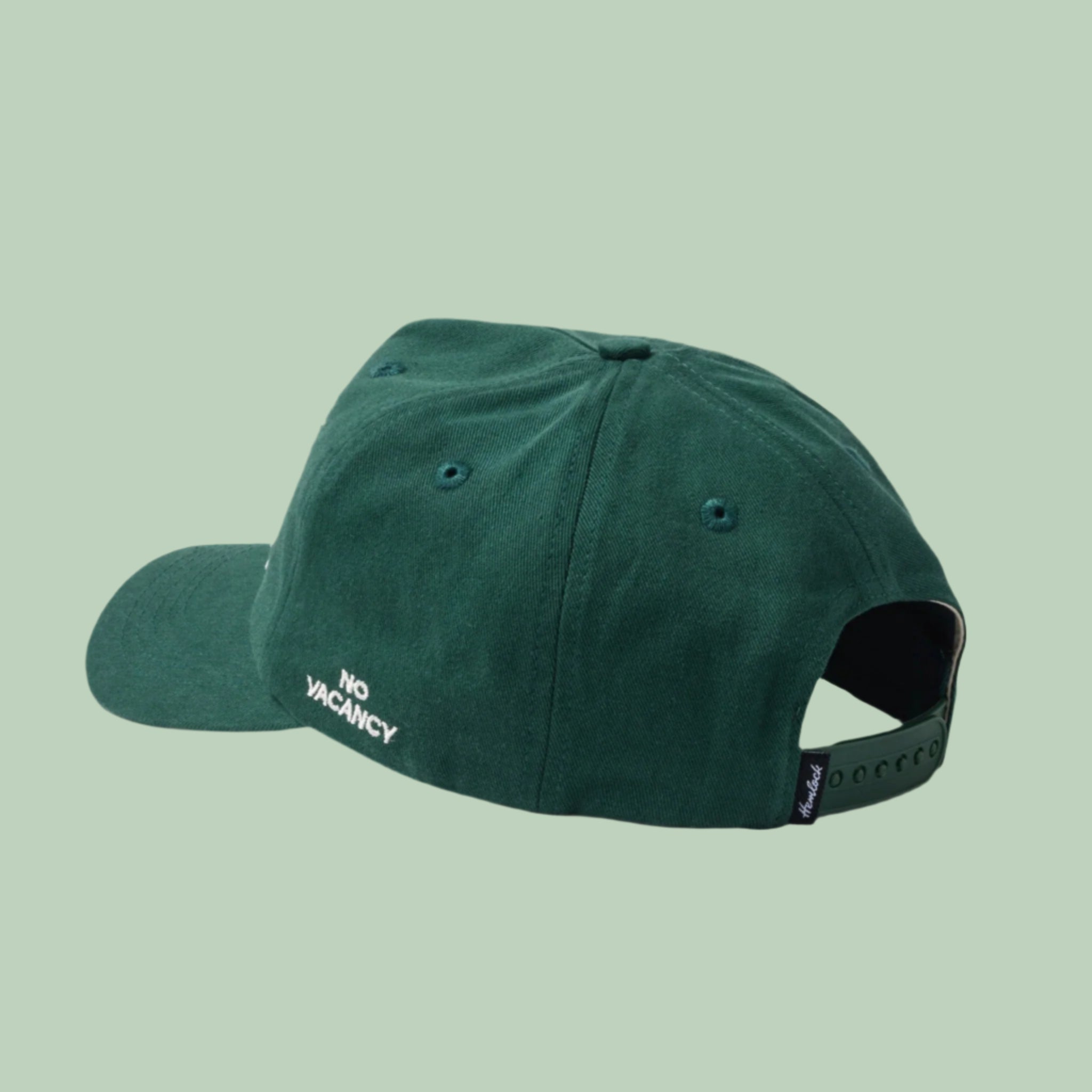 A dark green baseball hat with a snapback adjustable strap and white embroidered text on the side that reads, 'No Vacancy'. 