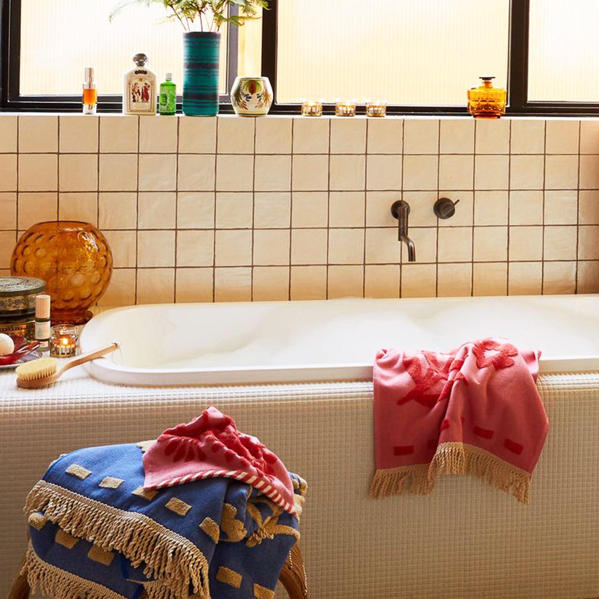 A light and dark pink hand towel with a floral pattern and fringe detailing on two ends. 