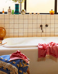 A light and dark pink hand towel with a floral pattern and fringe detailing on two ends. 