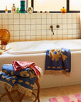A blue hand towel with a cream floral print design and fringe details on each end. 