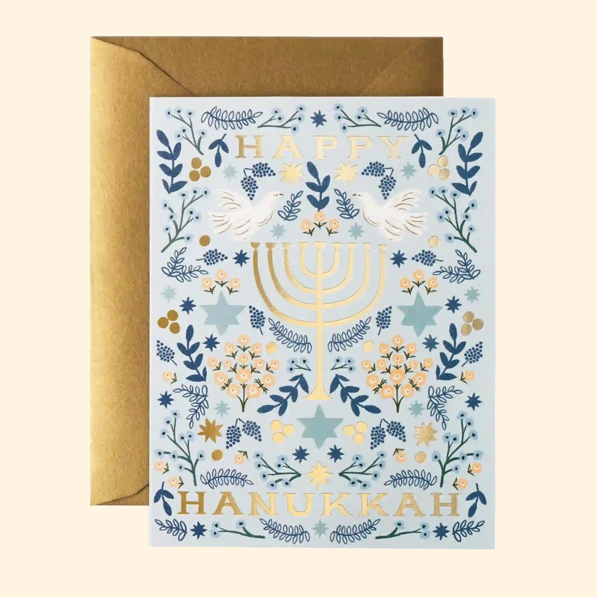 On a neutral background is a blue and white greeting card with gold fold text that reads, "Happy Hanukkah" along with a menorah graphic. 