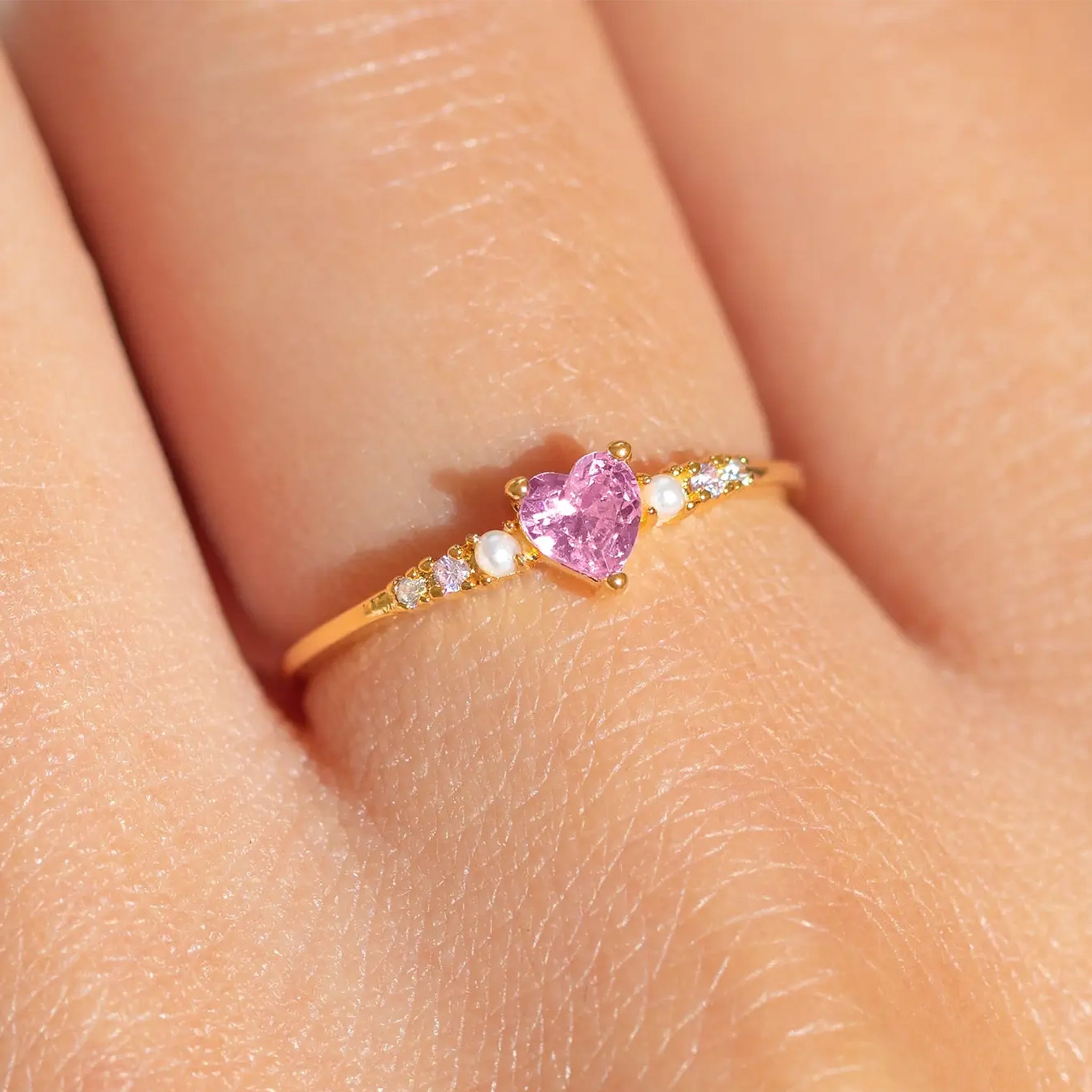 A gold ring with a pink heart shaped cz stone in the center. 