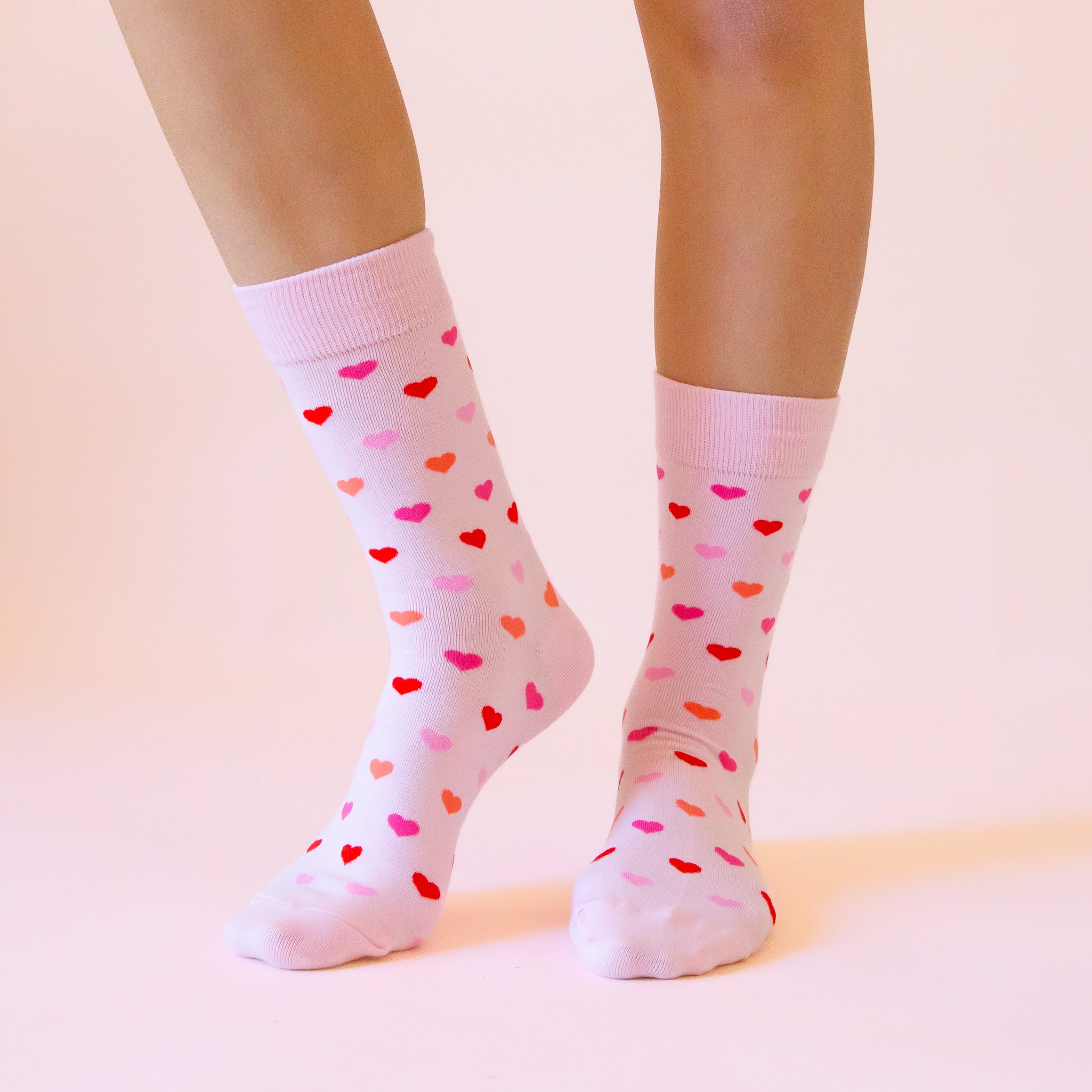 A  pair of crew socks with a heart print that is in different shades of pink. 