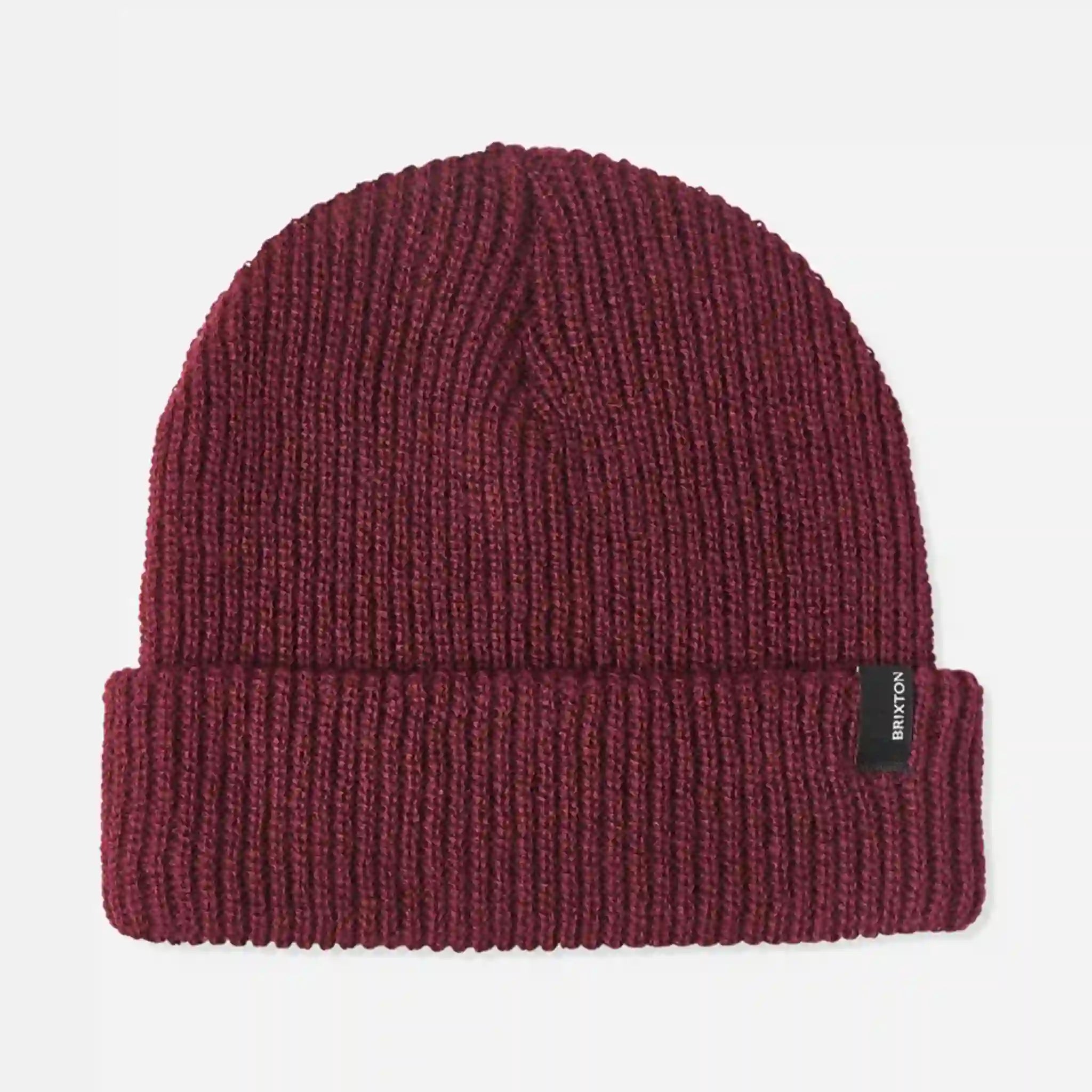 On a white background is a mahogany knit beanie with a black small label on the cuffed edge. 