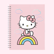 A pink spiral bound notebook with a graphic of Hello Kitty in the center standing on a multi colored rainbow. 