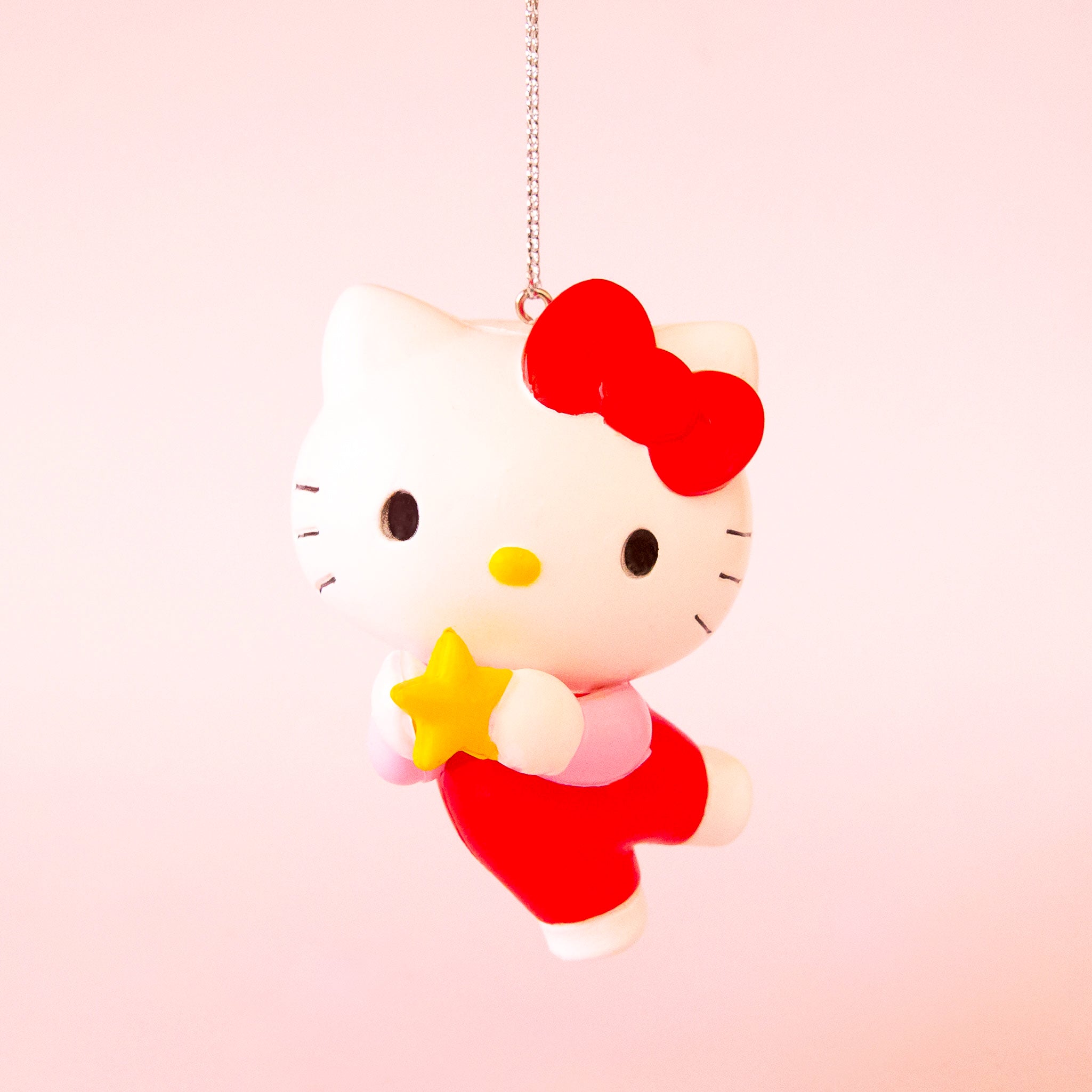 A hello kitty shaped ornament holding a star and wearing a red outfit with her signature red bow. 