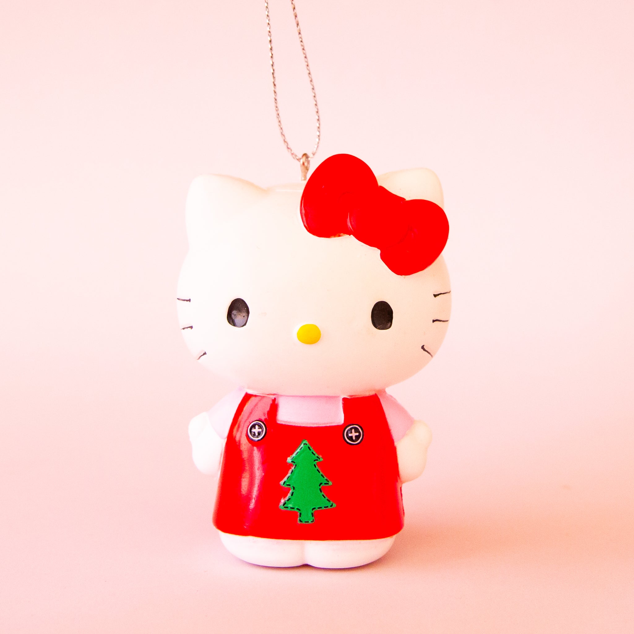 A Hello Kitty shaped ornament wearing a red outfit with a green Christmas tree in the center. 