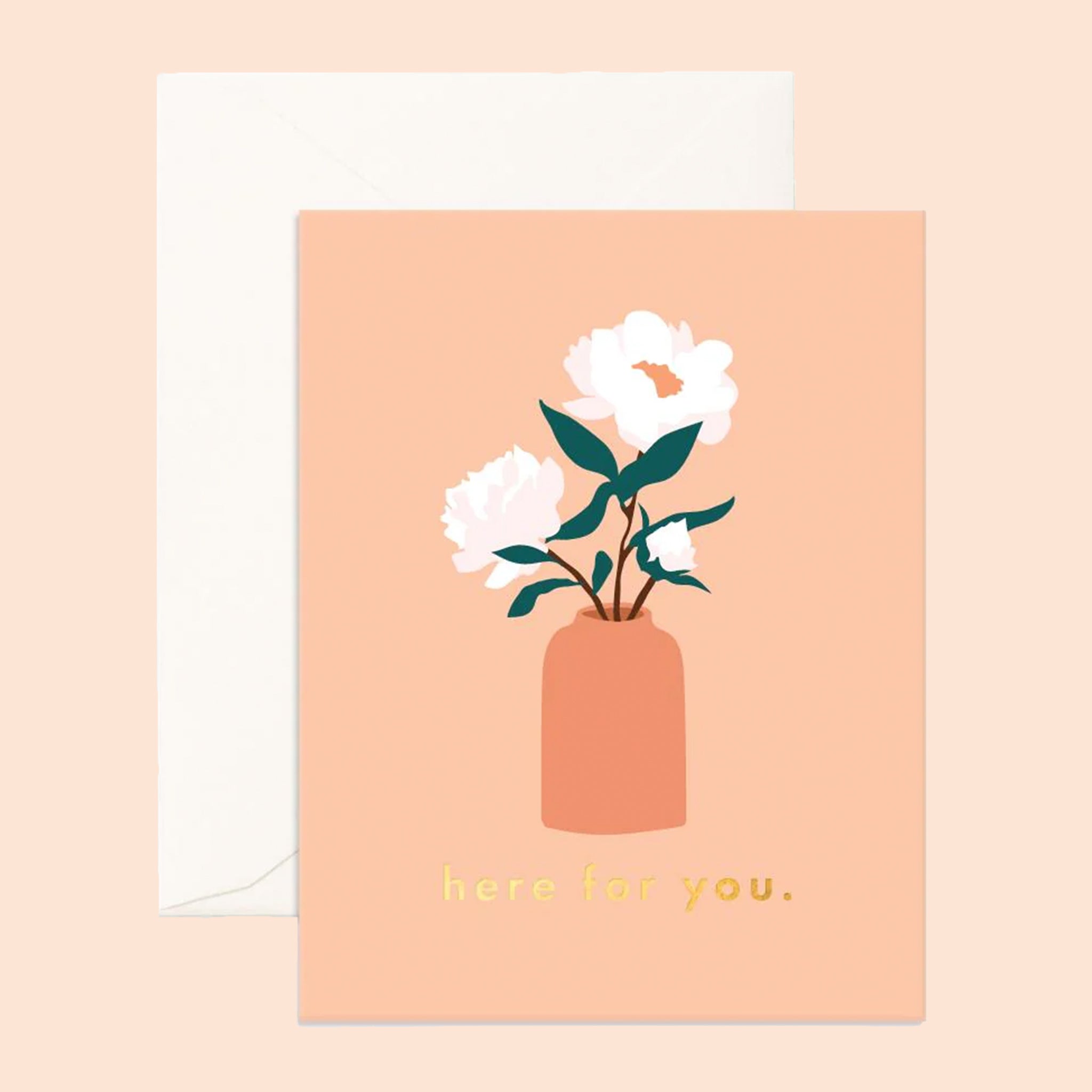 Photo of a peach greeting card on a white background. Greeting card reads &quot;here for you&quot; in lowercase, gold foil letters. There is an illustration of a coral colored vase with 3 white flowers with dark green stems above the writing. Envelope is white.
