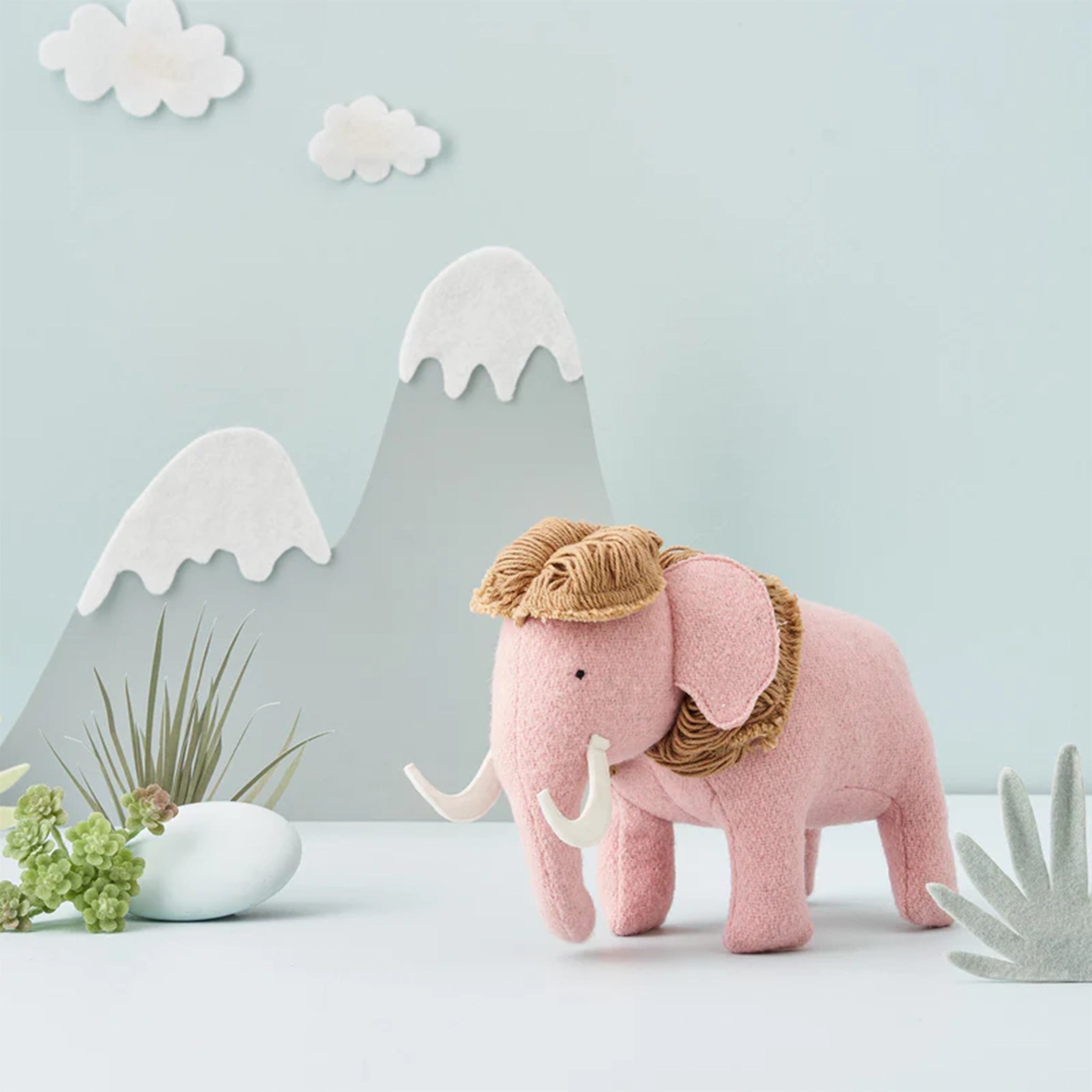 On a light blue background is a light pink mammoth stuffed toy. 