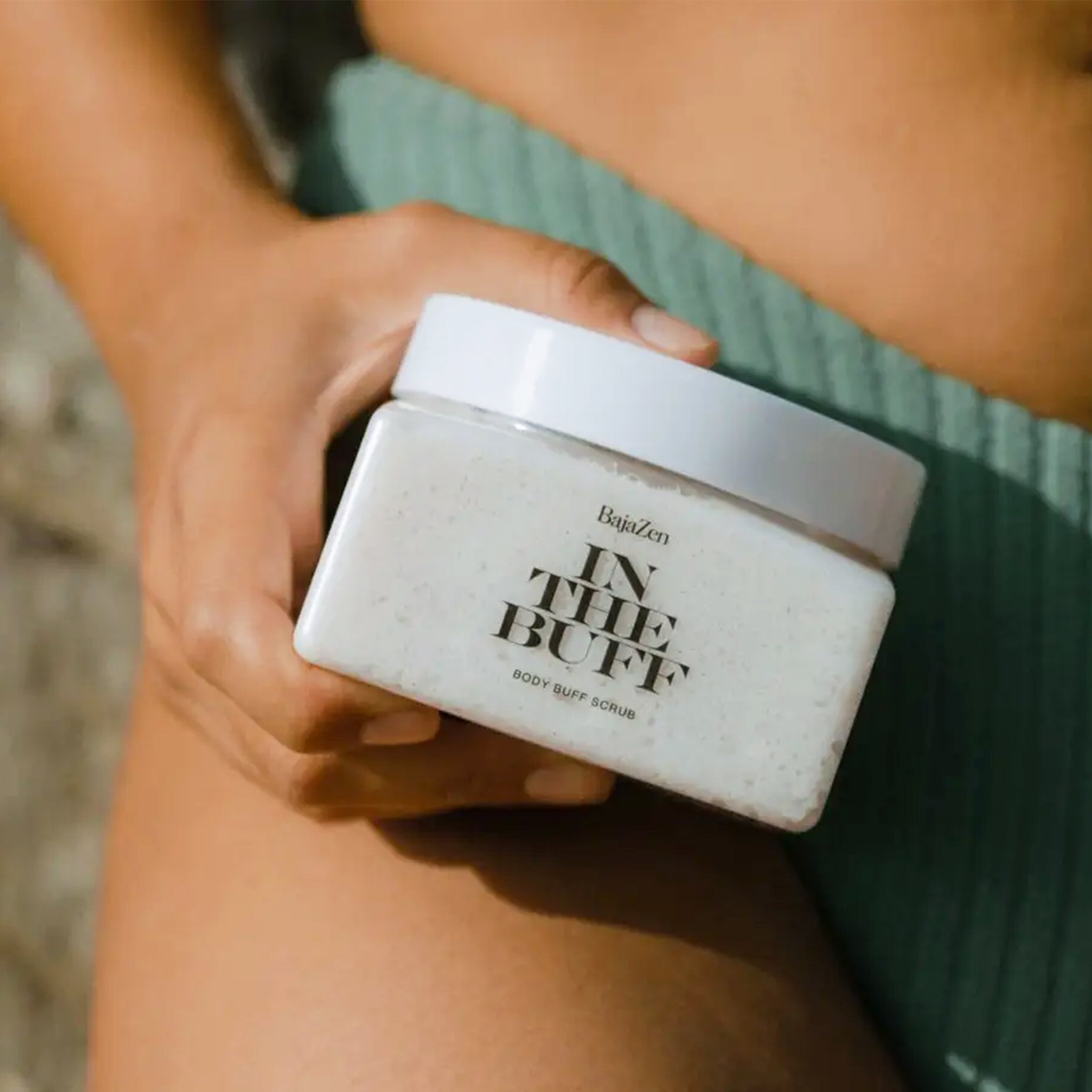 A clear container filled with a white body scrub with a white lid and black text that reads, "In The Buff Body Buff Scrub".