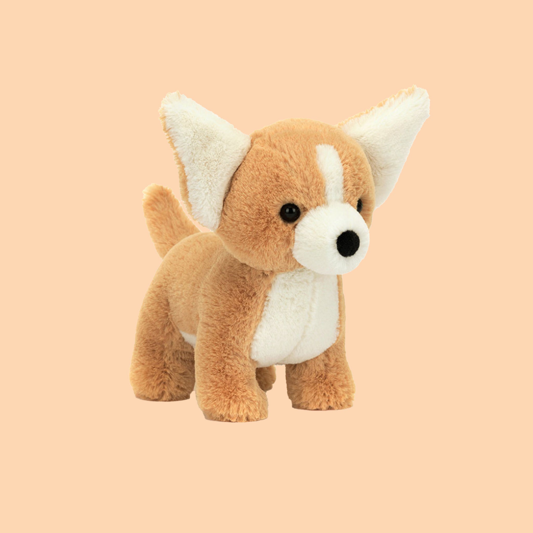 On a peachy background is a tan and white chihuahua shaped stuffed toy. 