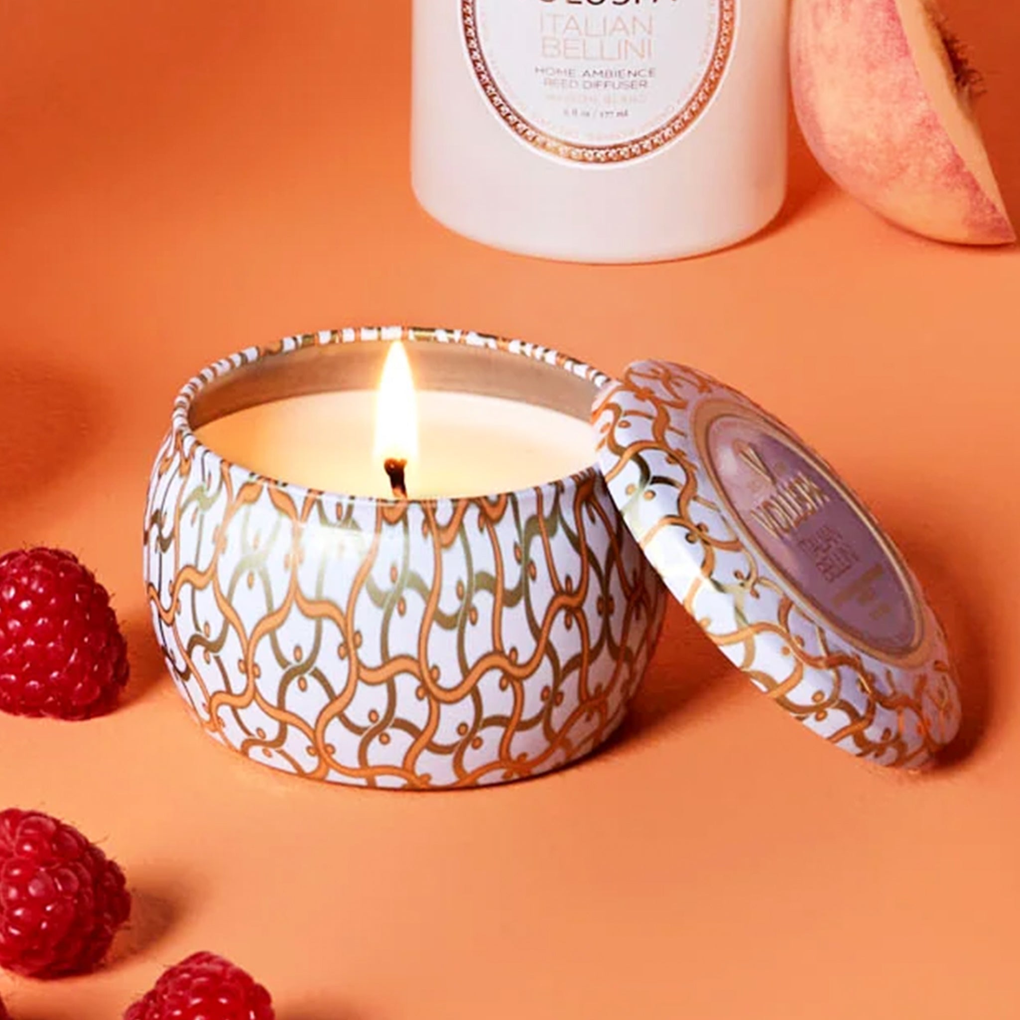 An orange and white tin that contains a single wick candle along with a circle label in the center of the lid that reads, "Voluspa Italian Bellini".