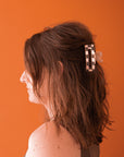 On an orange background is a model wearing the clear and ivory checker claw clip. 