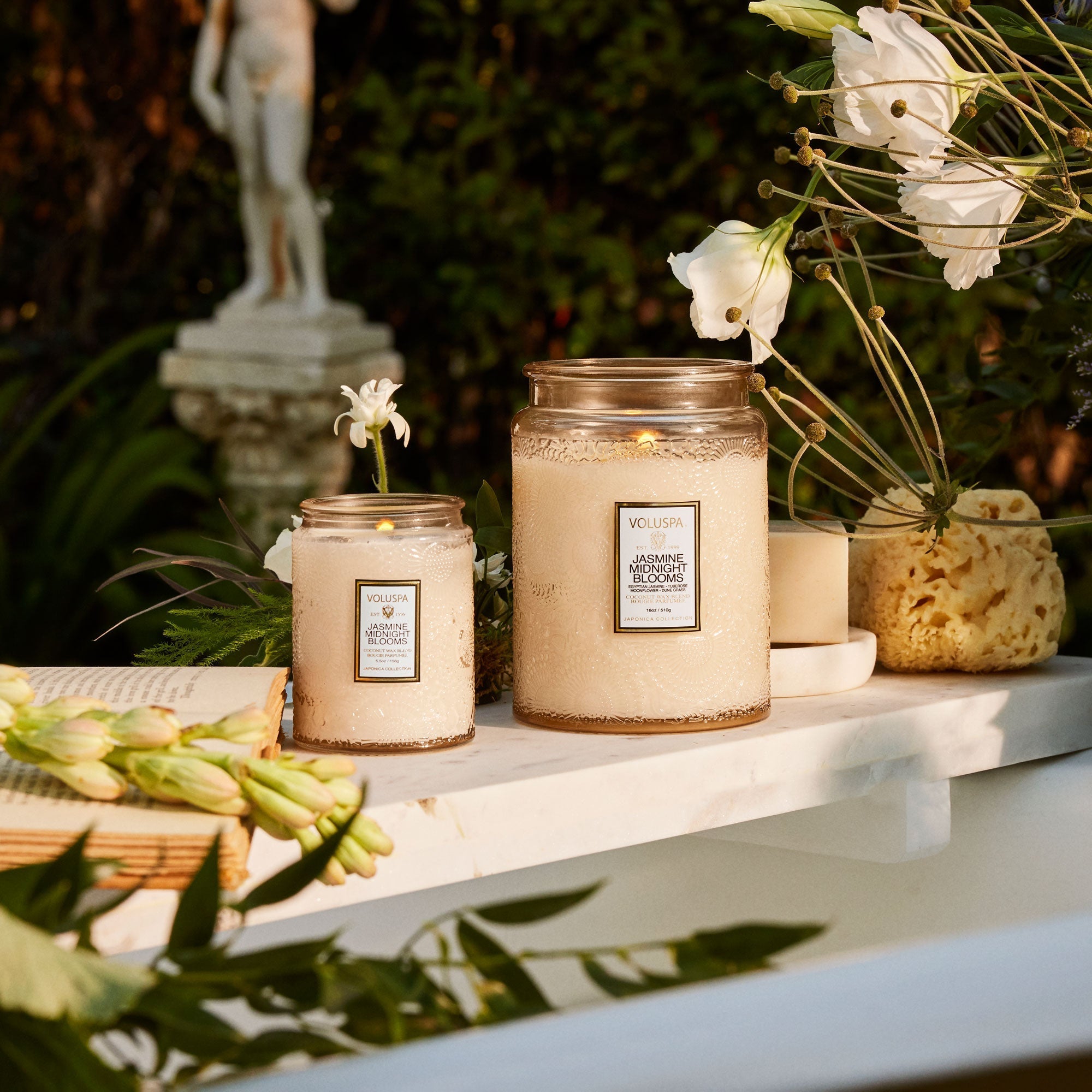 A decorative jar glass candle with a lid and label that reads, &quot;Jasmine Midnight Blooms&quot;. 