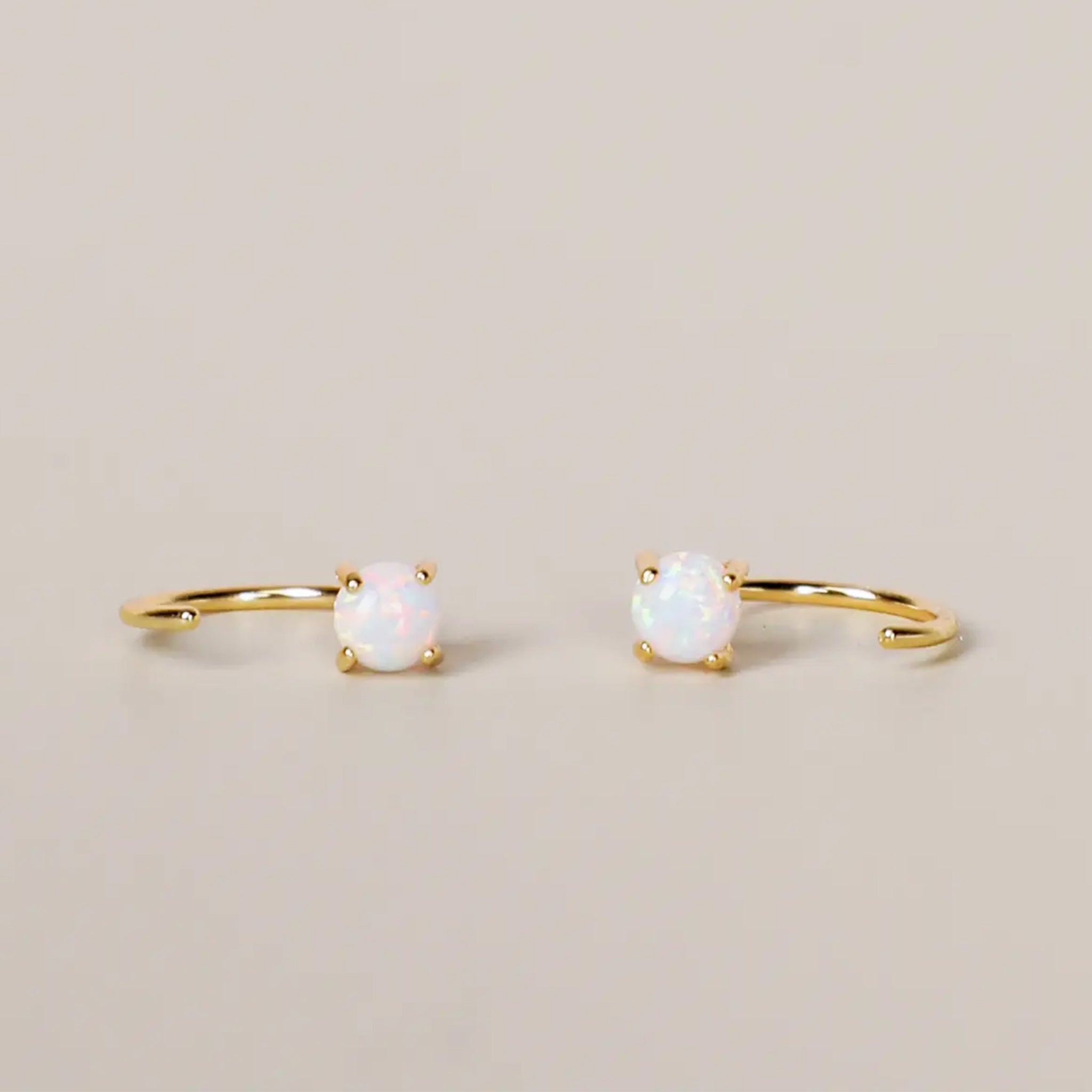 A pair of huggie hoop earrings with a small white opal stud. 