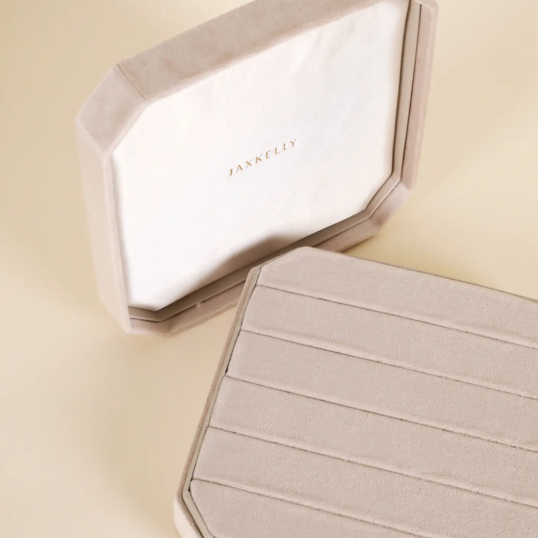 A cream velvet square jewelry box with slots for earrings and rings. 