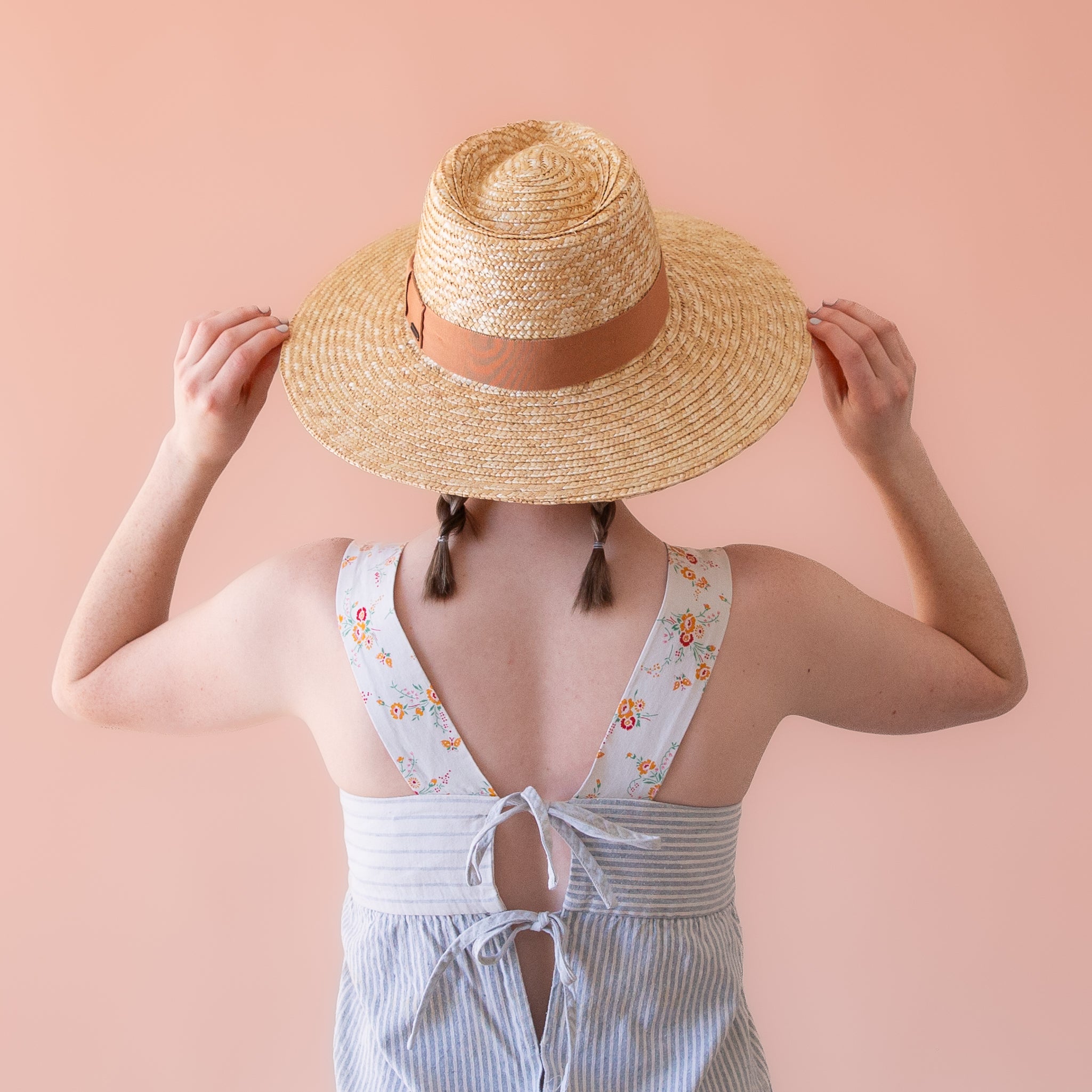 On a cream background is a light honey colored straw sun hat with a tan ribbon around the base.