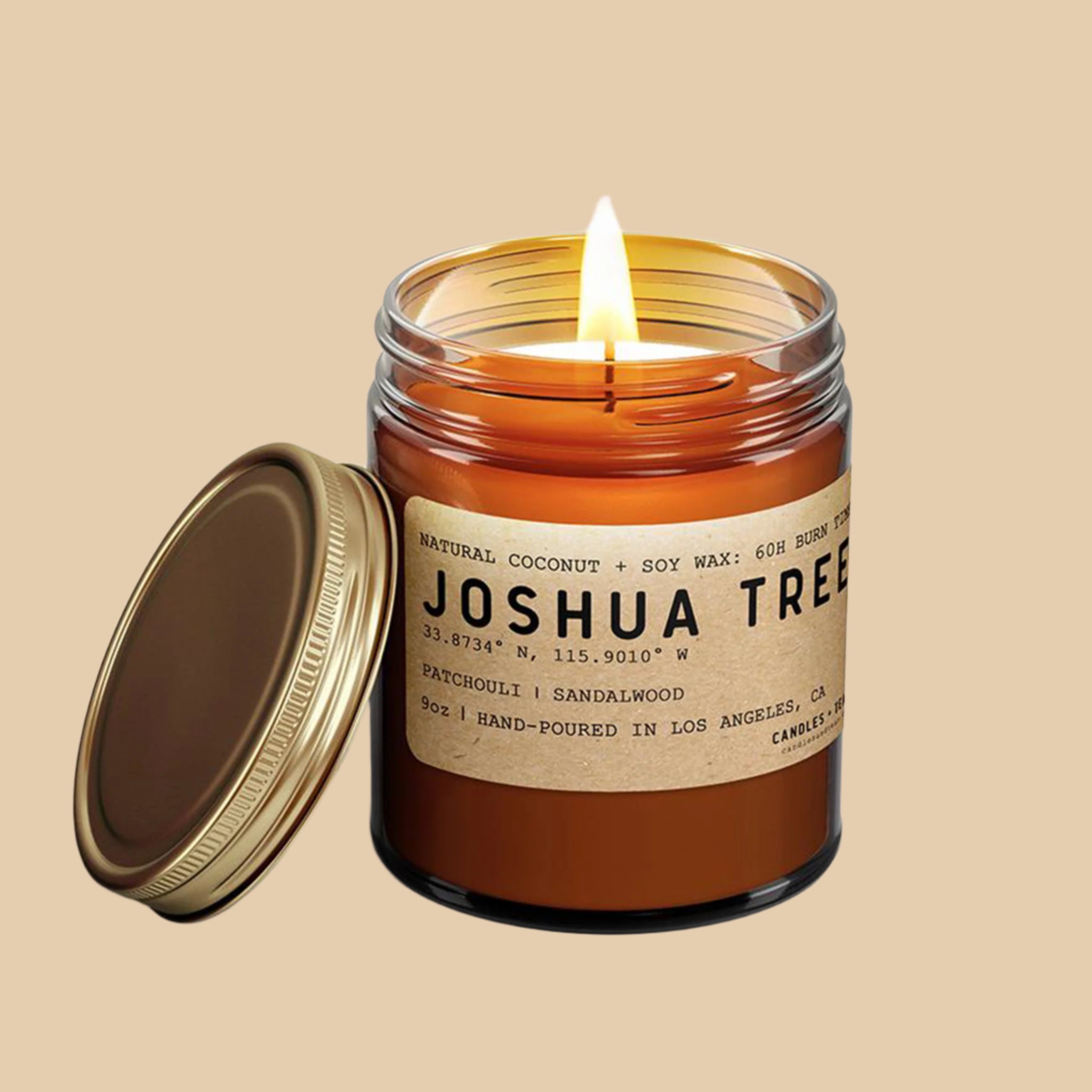 An amber colored glass candle jar with a brown label on the front that reads, "Joshua Tree Patchouli | Sandalwood" in black letter along with a single wick candle inside the jar and a gold screw on lid. 