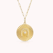 A gold chain necklace with a round pendant with a horseshoe shape design in the center with a cz stone. 