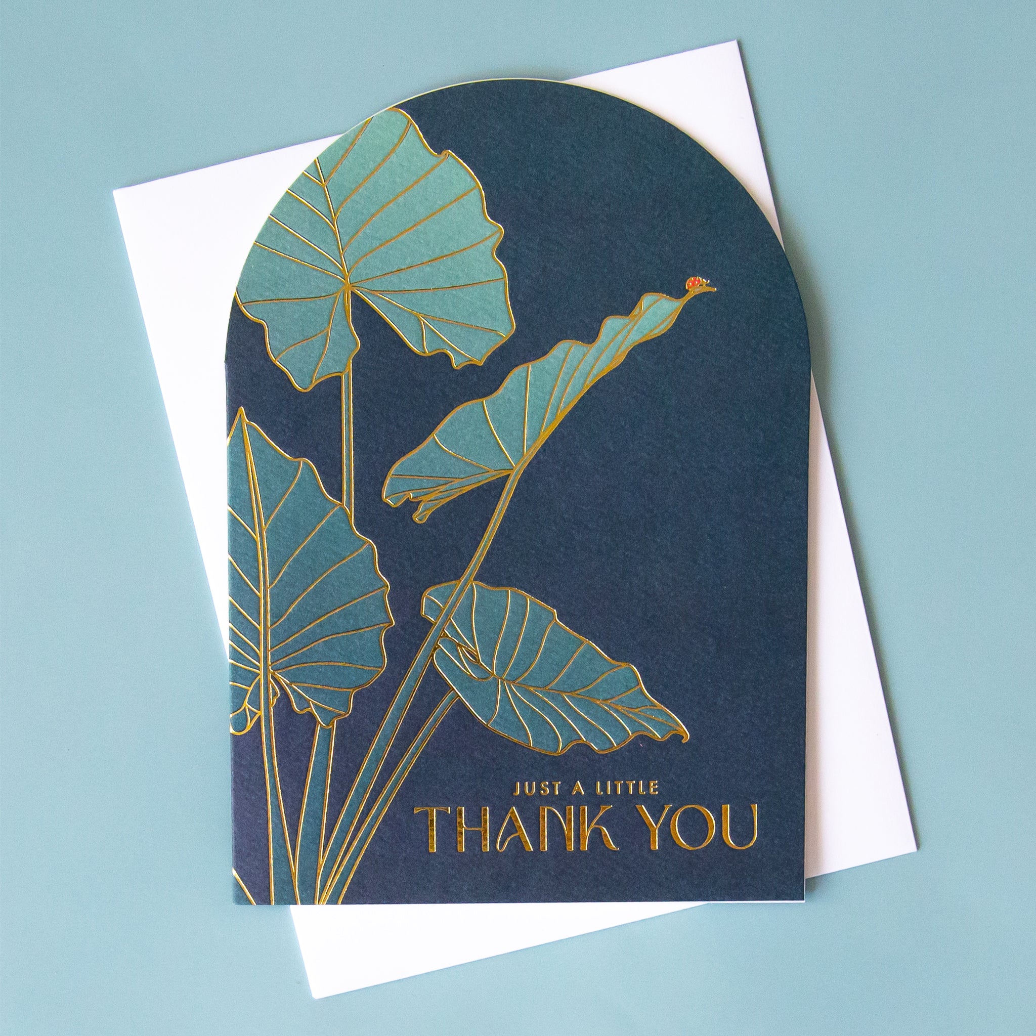 A blue arched shape card with a plant illustration on the front and gold foiled text that reads, &quot;Just A Little Thank You&quot;.