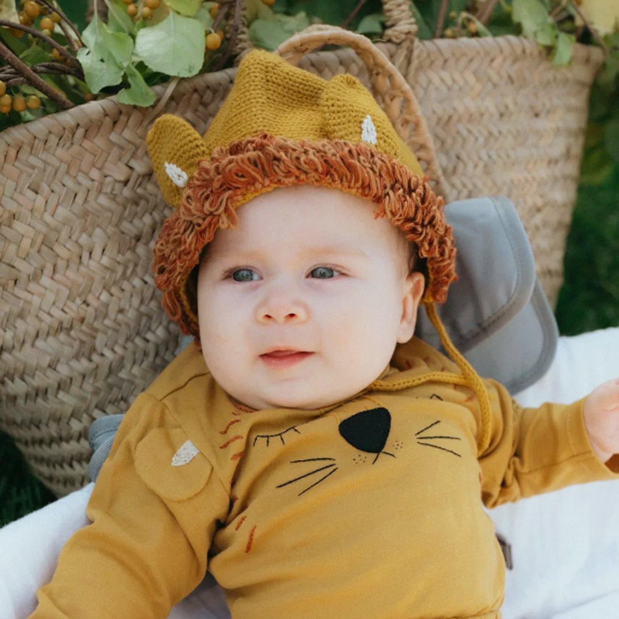 A mustard yellow knitted bonnet with a tie at the bottom and shaped like a lion's mane. 