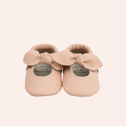 Baby moccasins made of soft leather in a light pink shade with a bow on the top. 