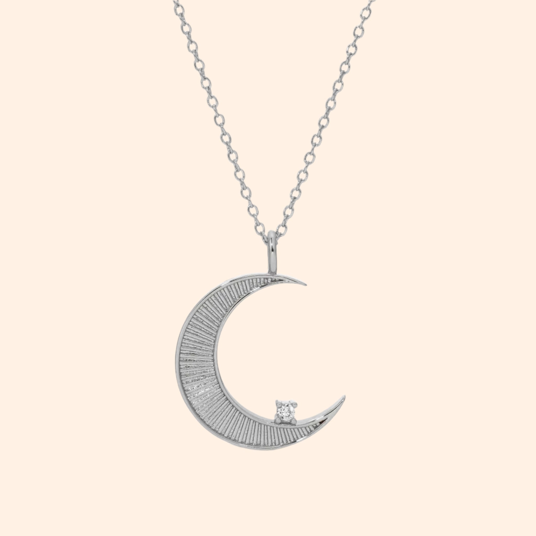 A gold necklace with a moon shaped pendant and a cz stone on the edge. 