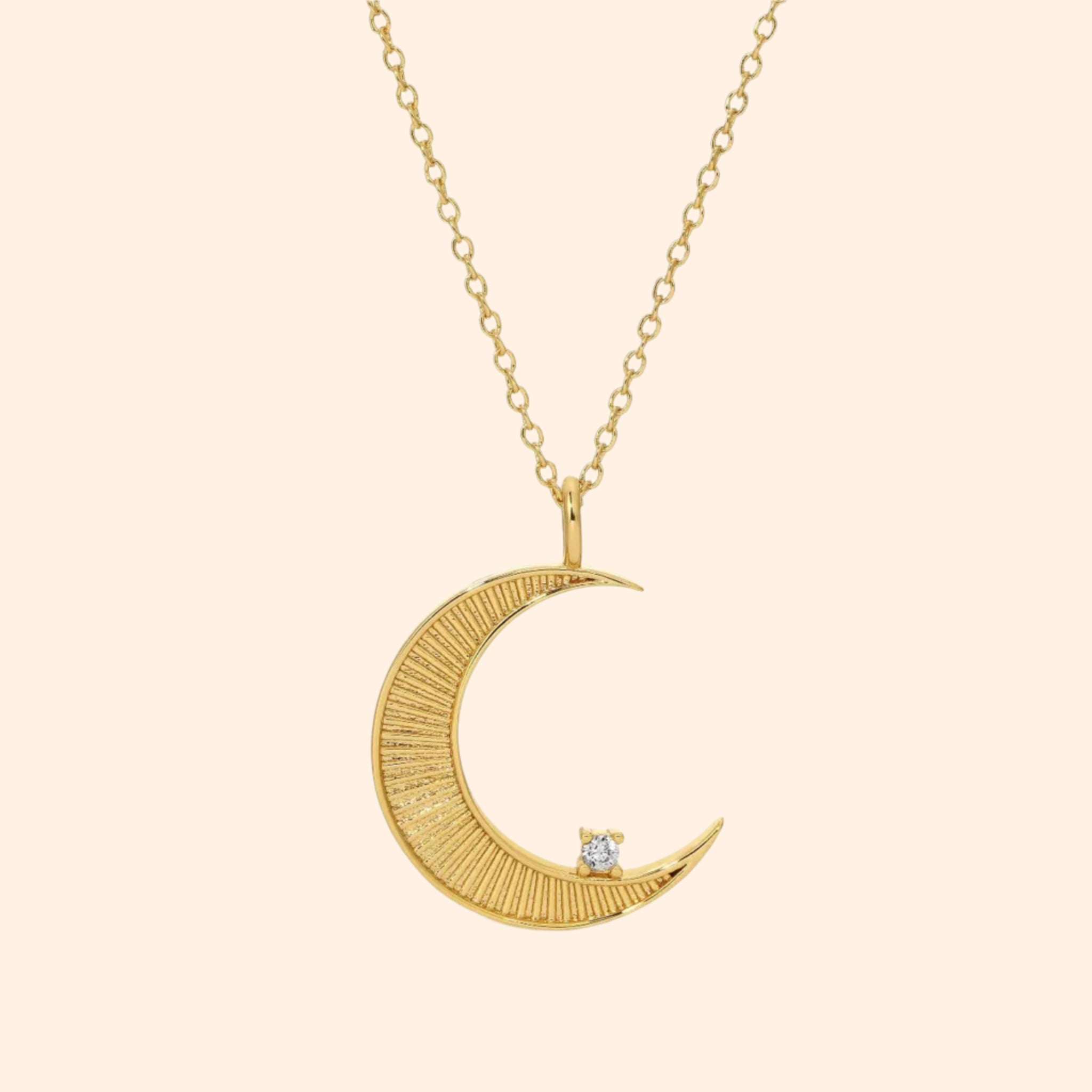 A gold necklace with a moon shaped pendant and a cz stone on the edge. 